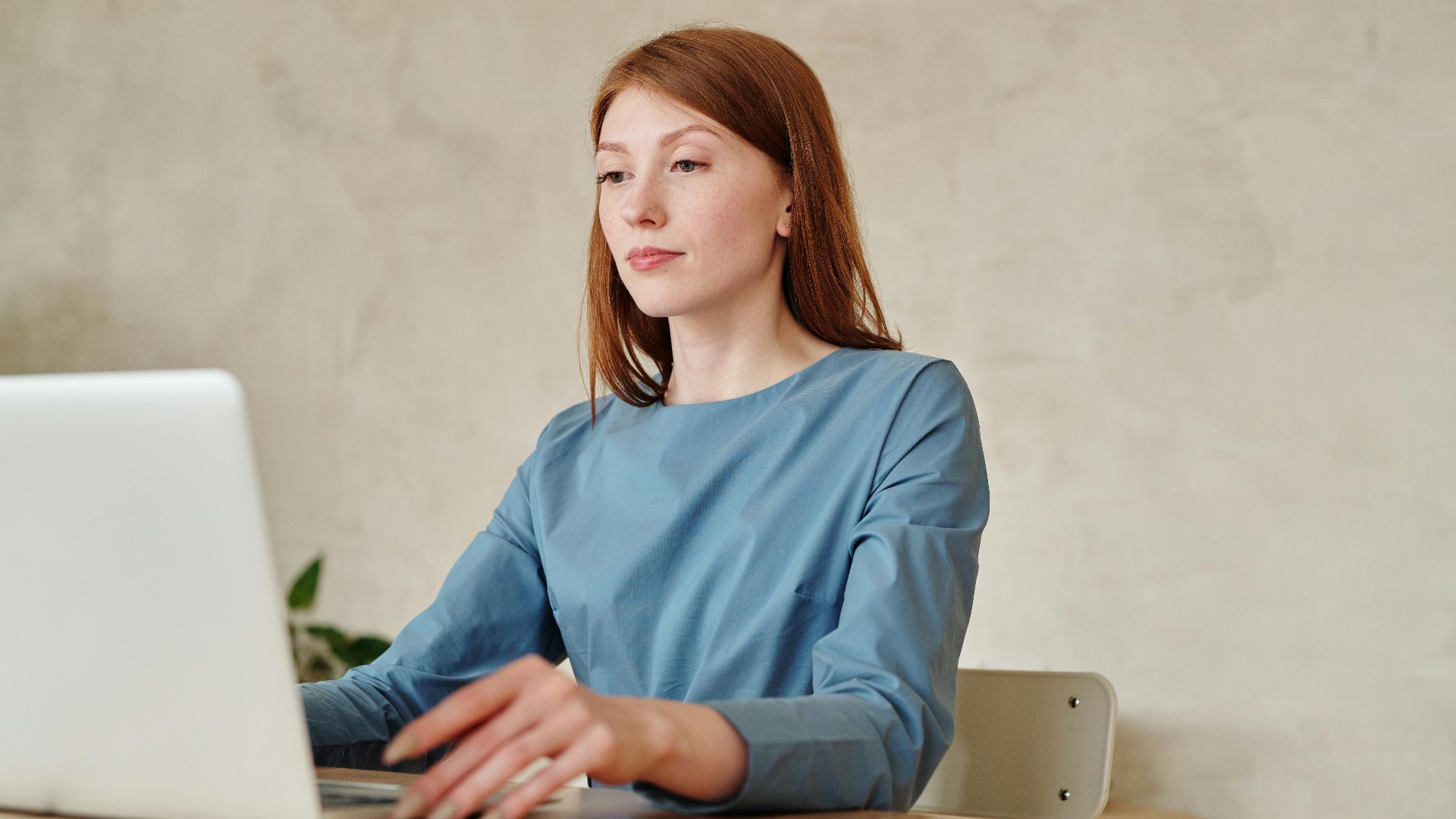 Caucasian woman in blue shirt working on a laptop indoors at home.