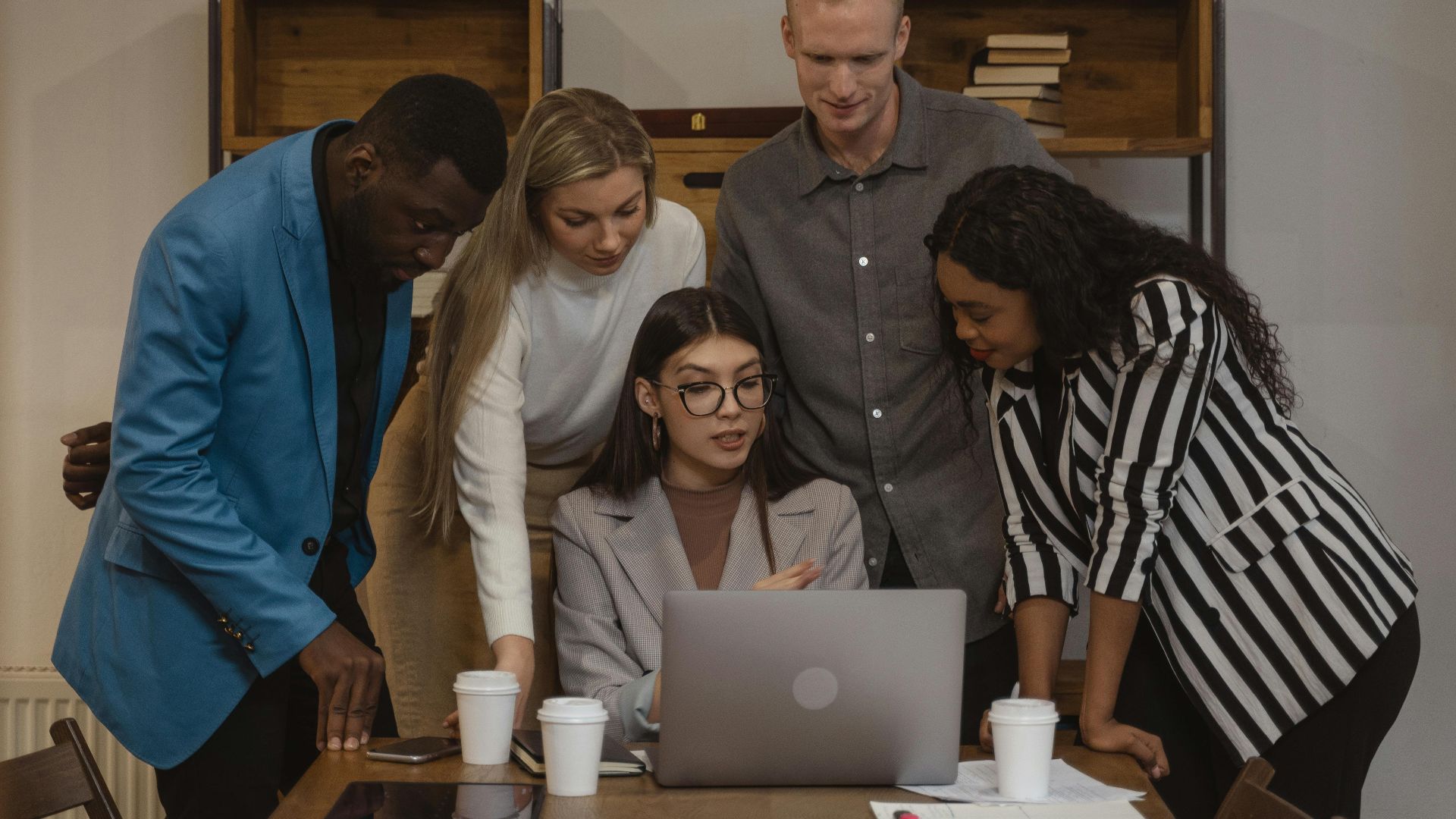 A diverse group of colleagues engaged in teamwork around a laptop during a planning session.