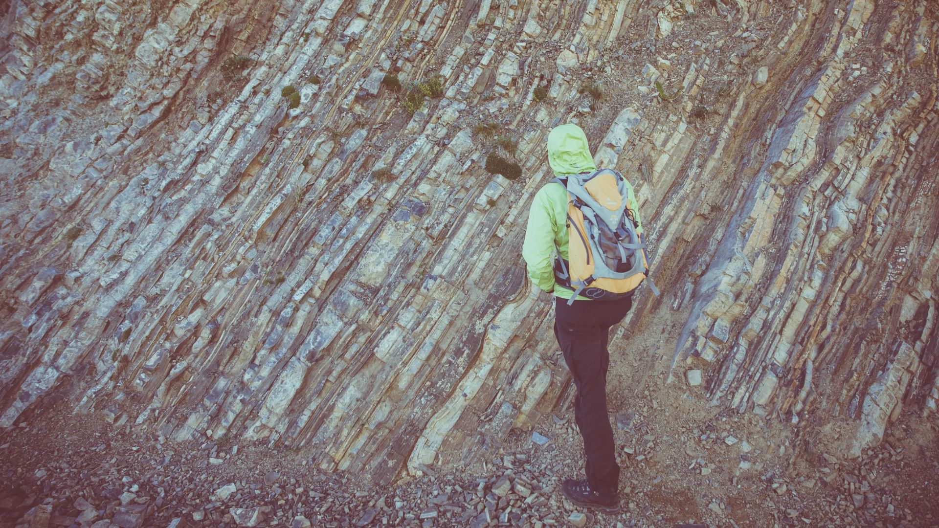 A lone hiker with a backpack explores the rugged and textured rocky mountain surface.