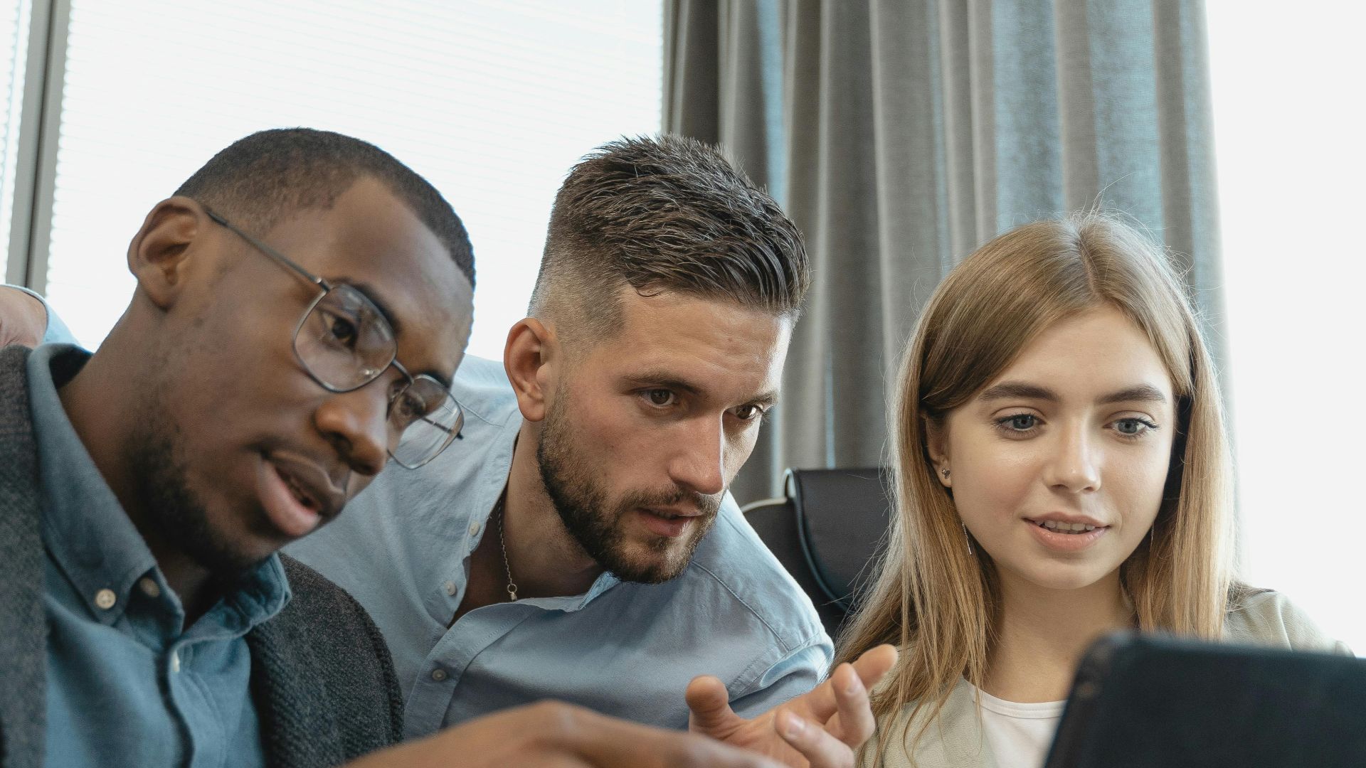 A diverse group of professionals working together on a digital tablet in an office.