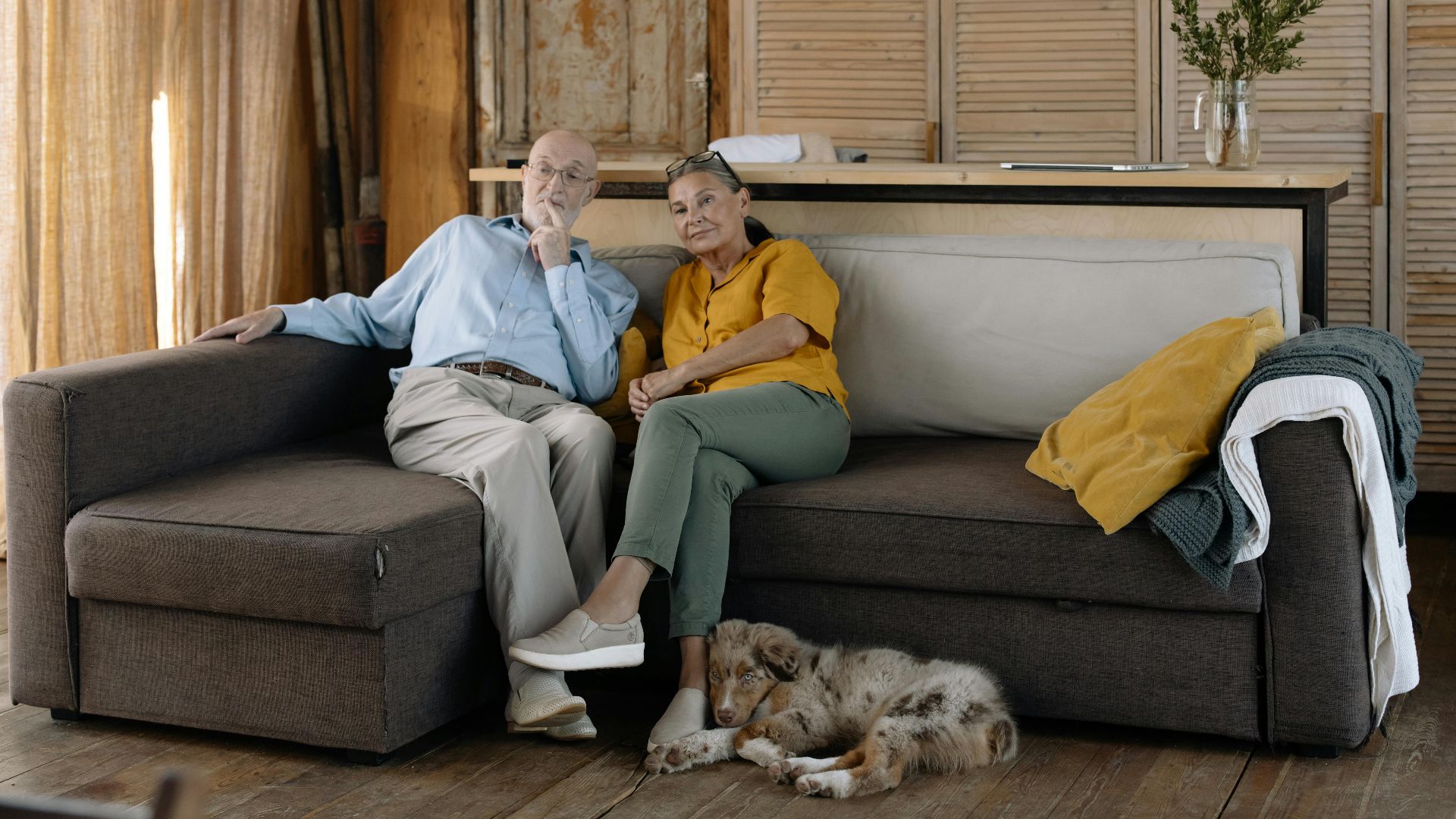Charming scene of an elderly couple enjoying a cozy moment with their dog on a sofa in a rustic home.