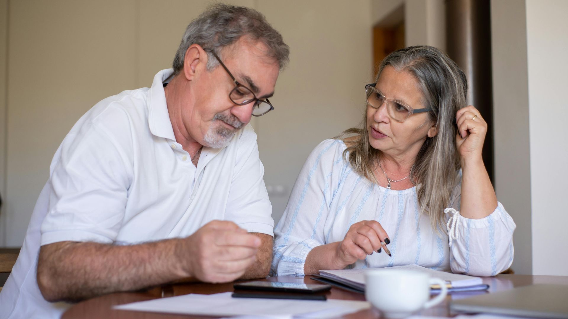 Senior couple reviewing documents and managing finances together at home, showing collaboration and care.