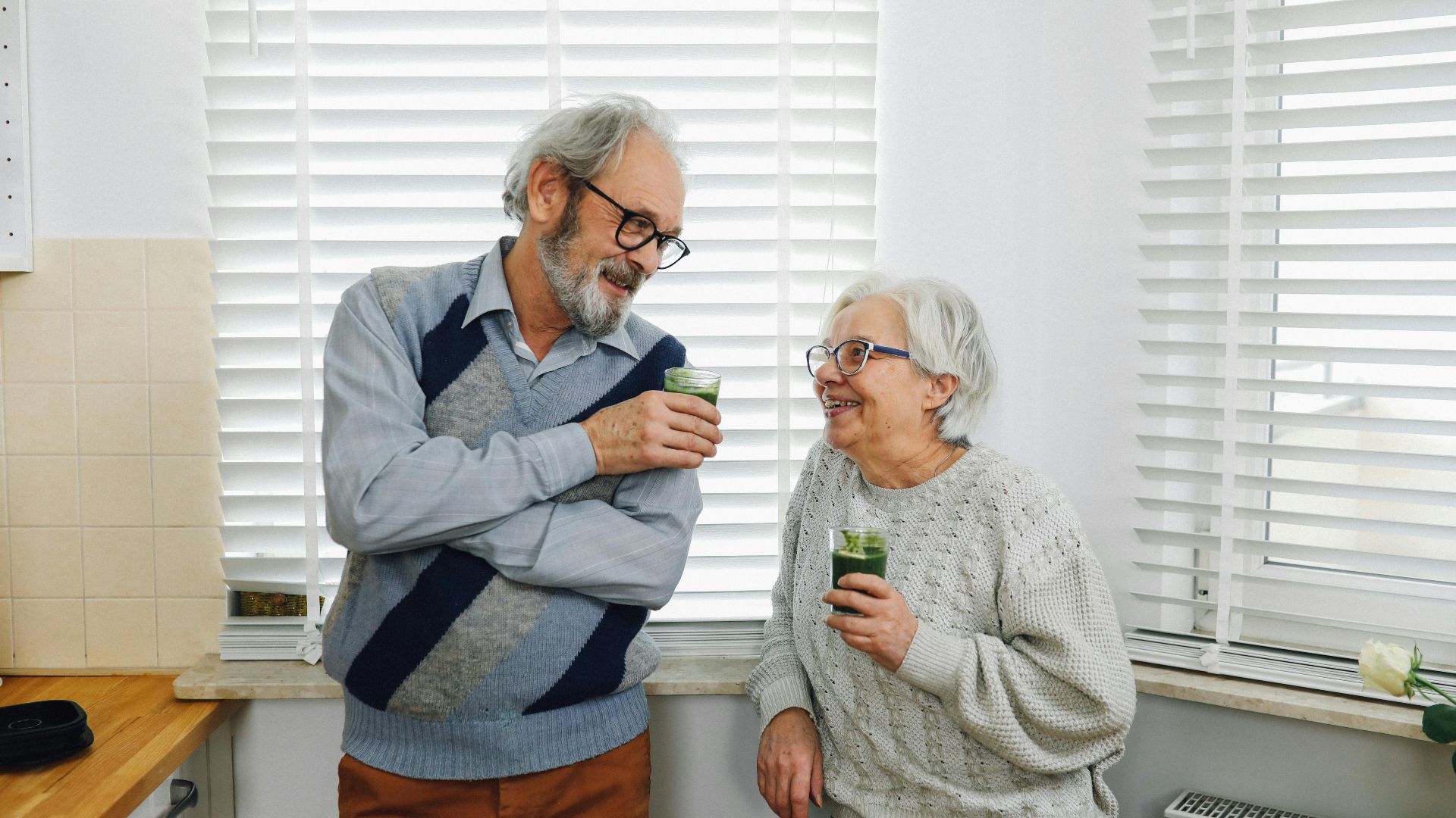 Senior couple smiling and enjoying green smoothies in a cozy kitchen setting.