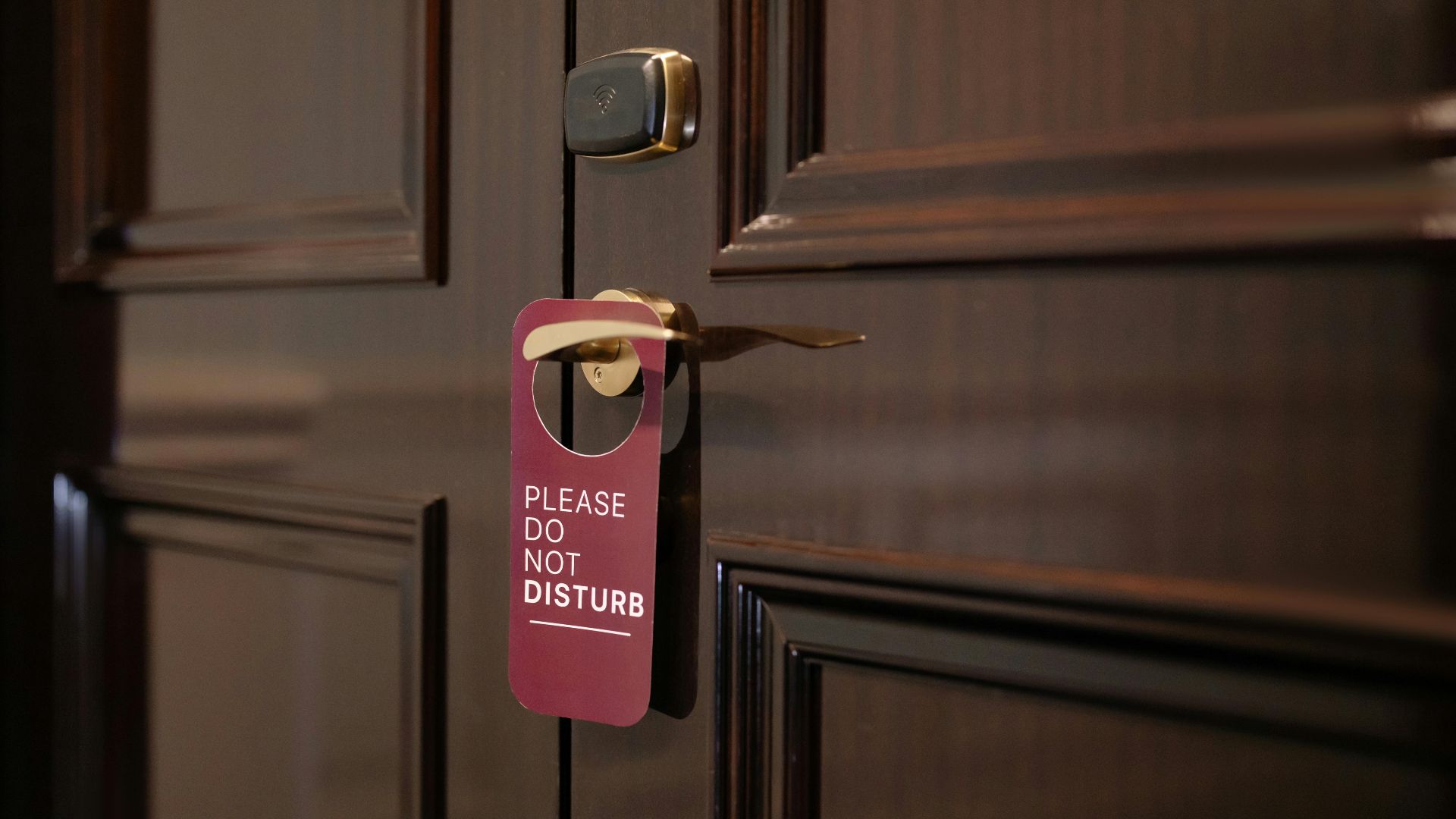 A wooden hotel door with a 'Please Do Not Disturb' sign hanging on the handle.