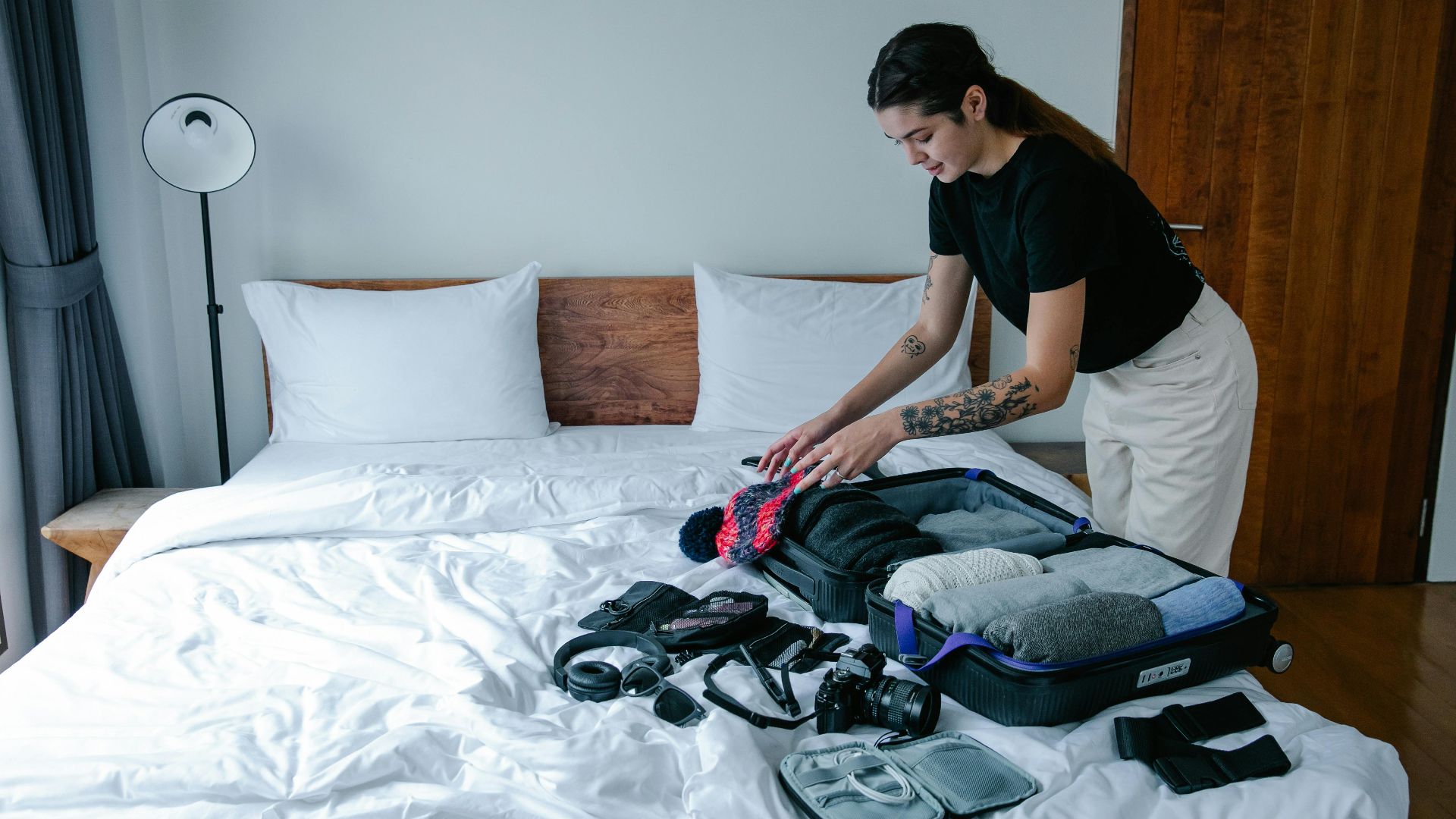 Young woman organizing luggage on a bed in a stylish indoor setting, preparing for travel.