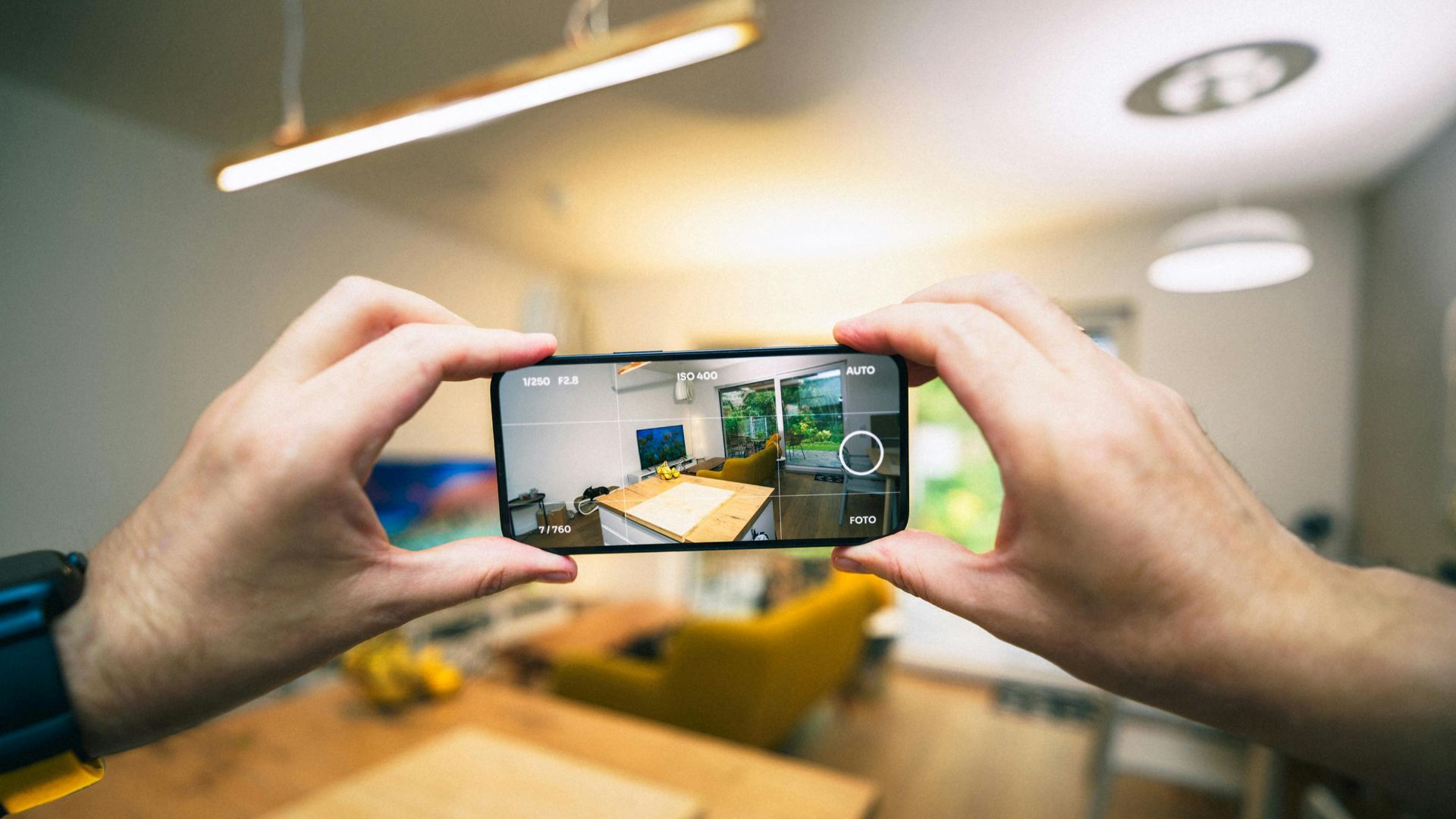 Hands capturing a modern living room interior with a smartphone.