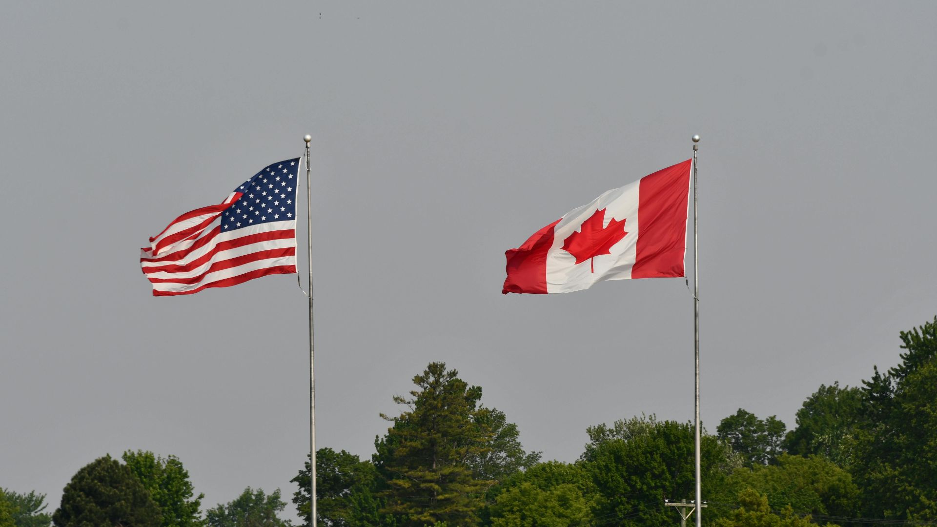 Flags of the USA and Canada waving on flagpoles against a clear sky in Sarnia, Ontario.