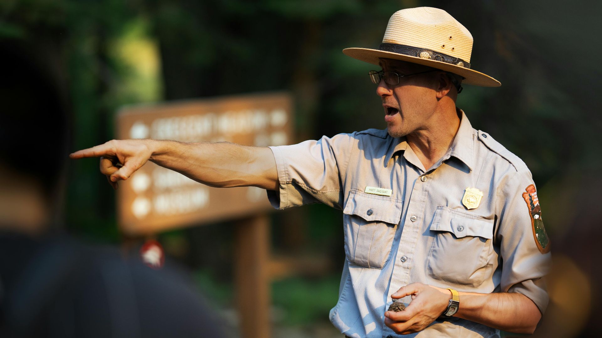 Park ranger guiding a group through a forest area, pointing with emphasis.