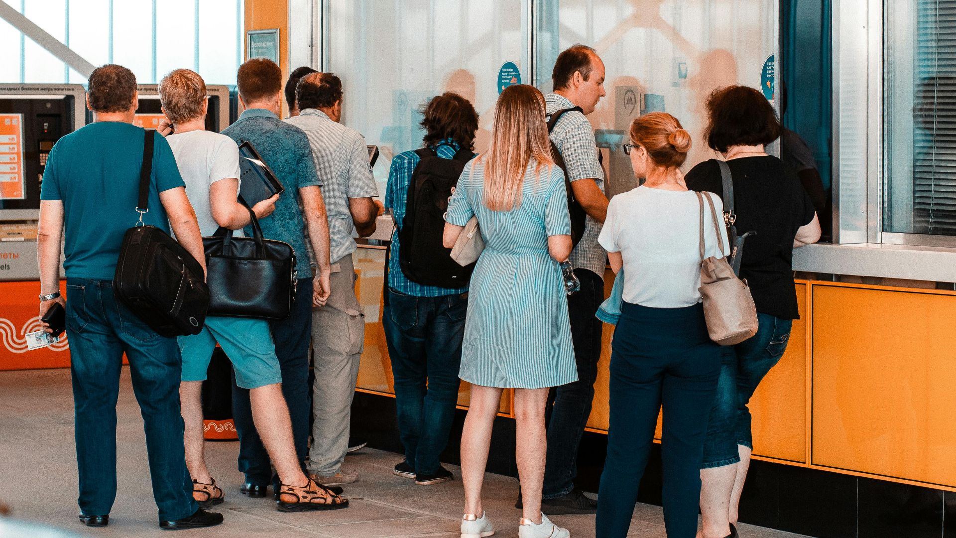 Back view of unrecognizable people in casual wear standing near ticket office in public place