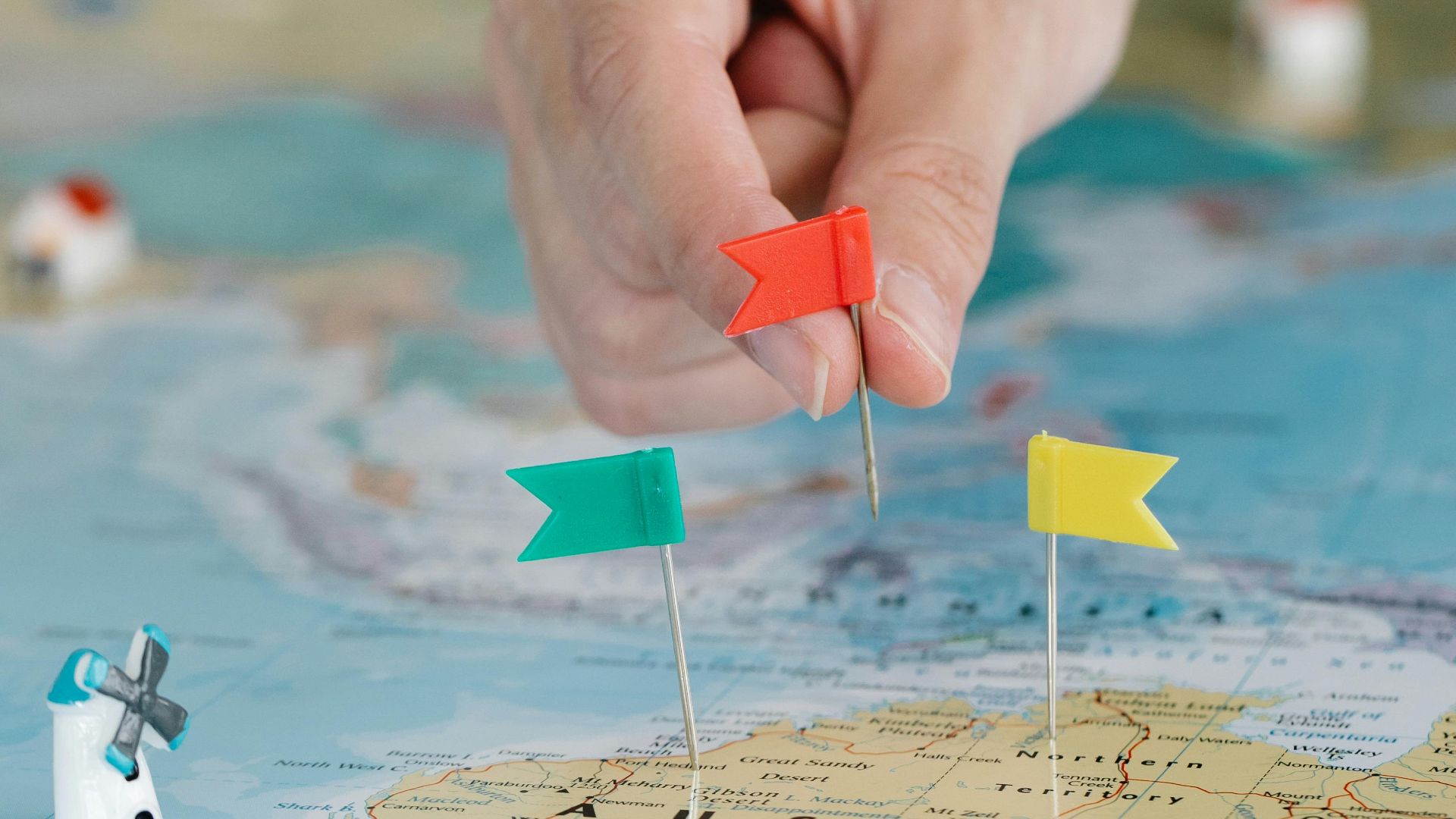 Close-up of a hand pinning flags on a map for trip planning and exploration.