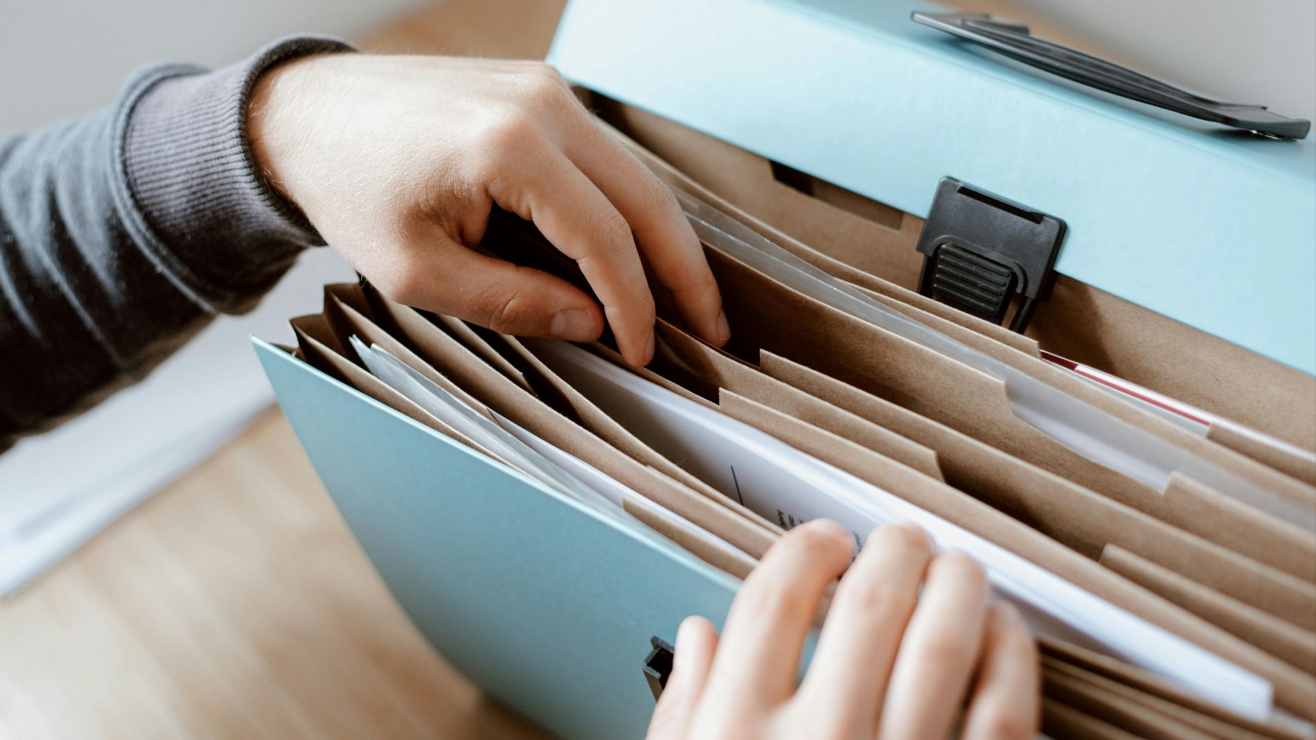 Crop unrecognizable person selecting document in opened briefcase for documents placed on wooden table