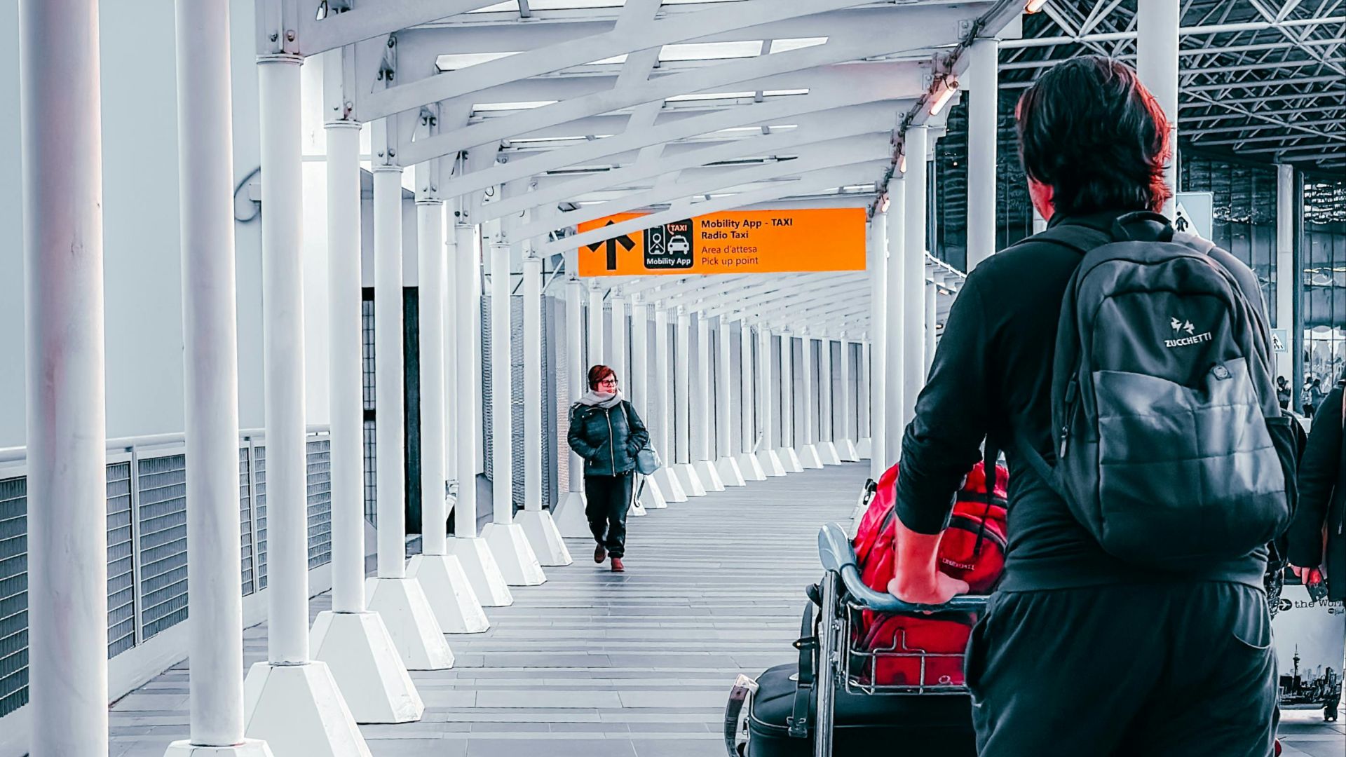 Travelers with luggage trolleys navigating through Dortmund Airport's terminal walkway.