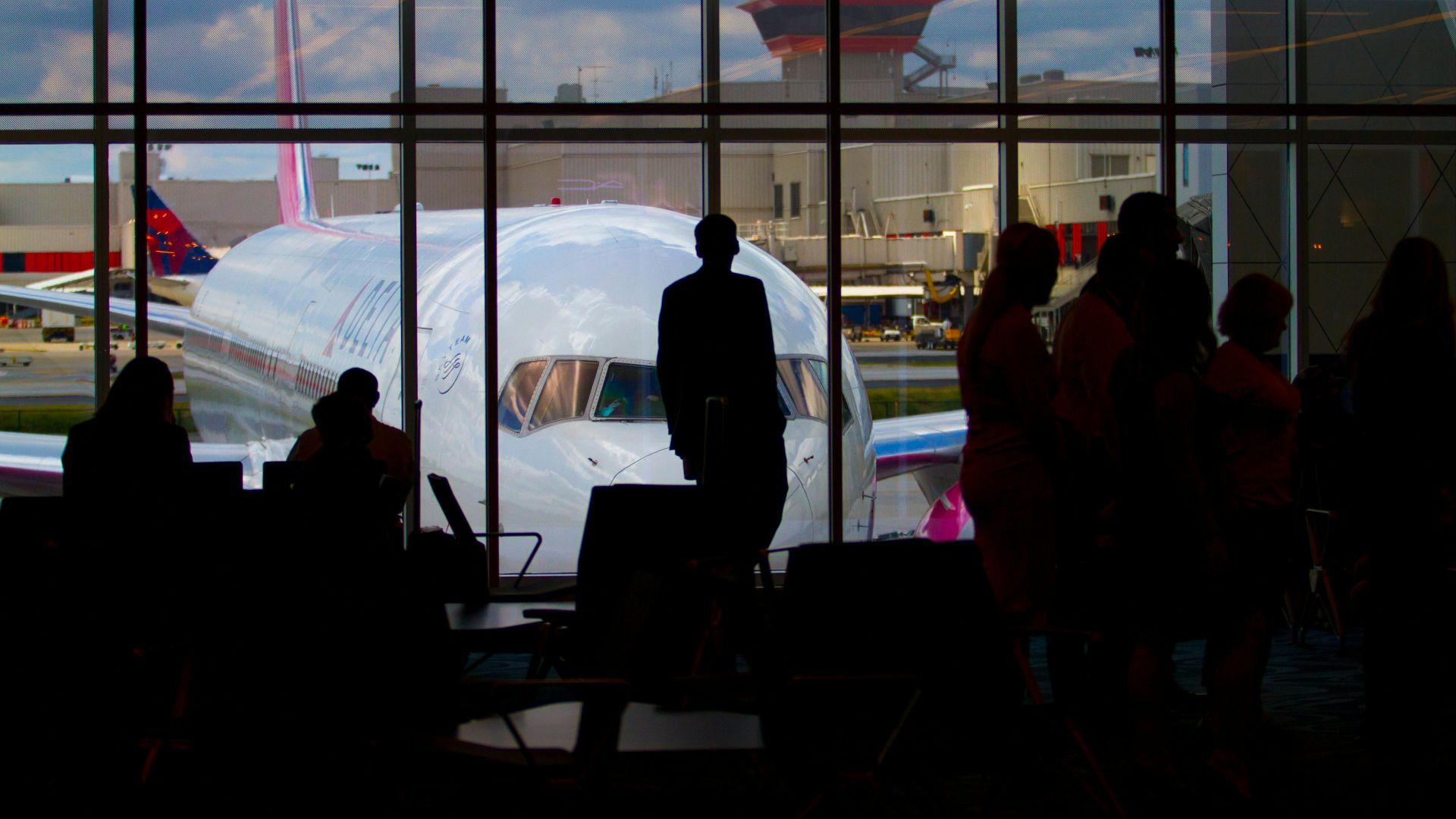 Silhouettes of travelers waiting at an airport terminal with an airplane visible through the window.