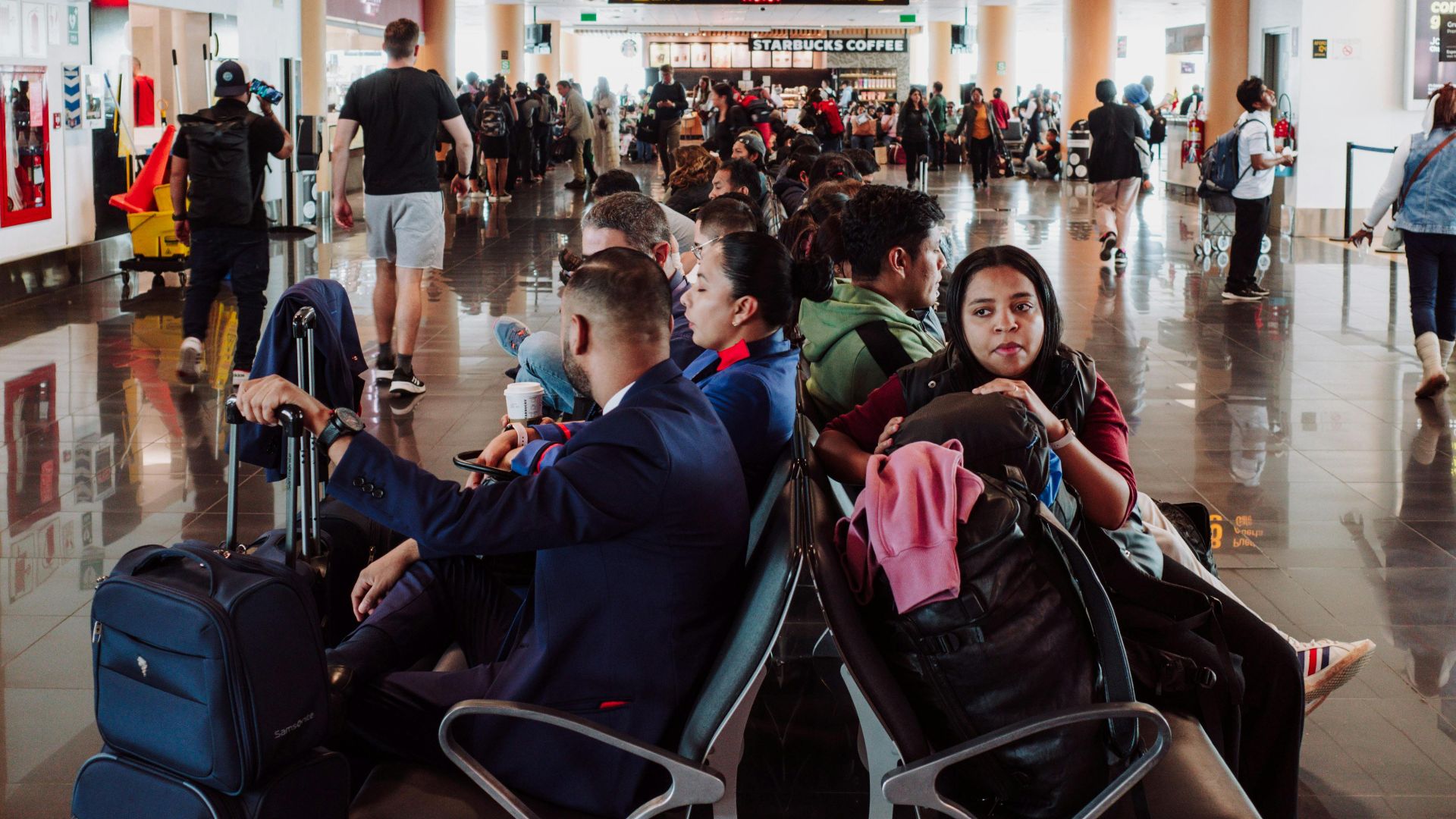 Passengers waiting in a busy airport terminal seating area, with luggage in the modern airport.
