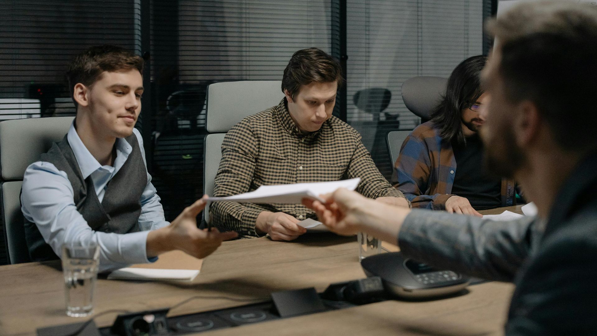 Four professionals exchanging documents during a meeting in an office setting.