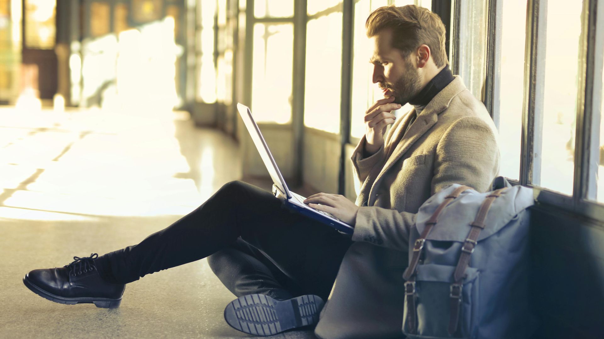 Young man sitting indoors at an airport using laptop. Ideal for remote work themes.