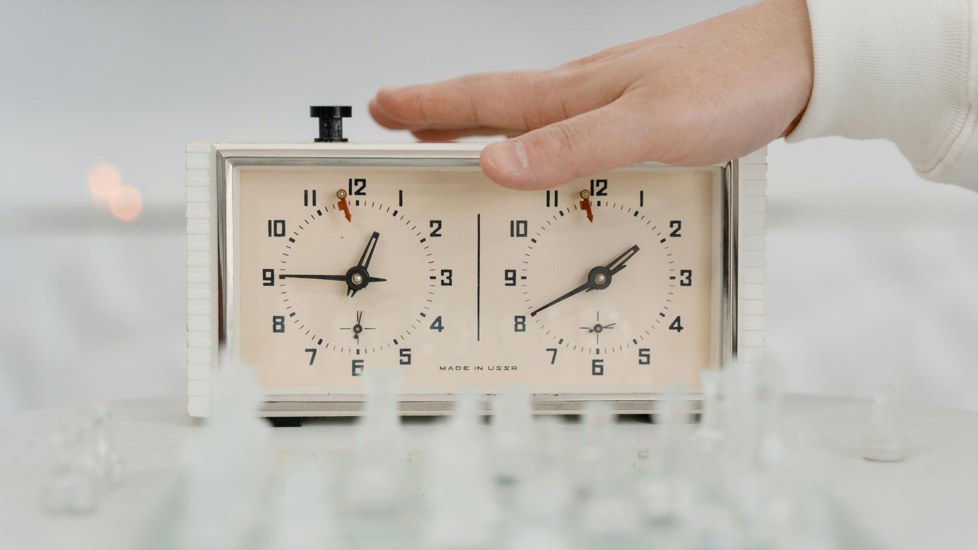 Close-up of a hand adjusting a chess clock during a timed chess game indoors.