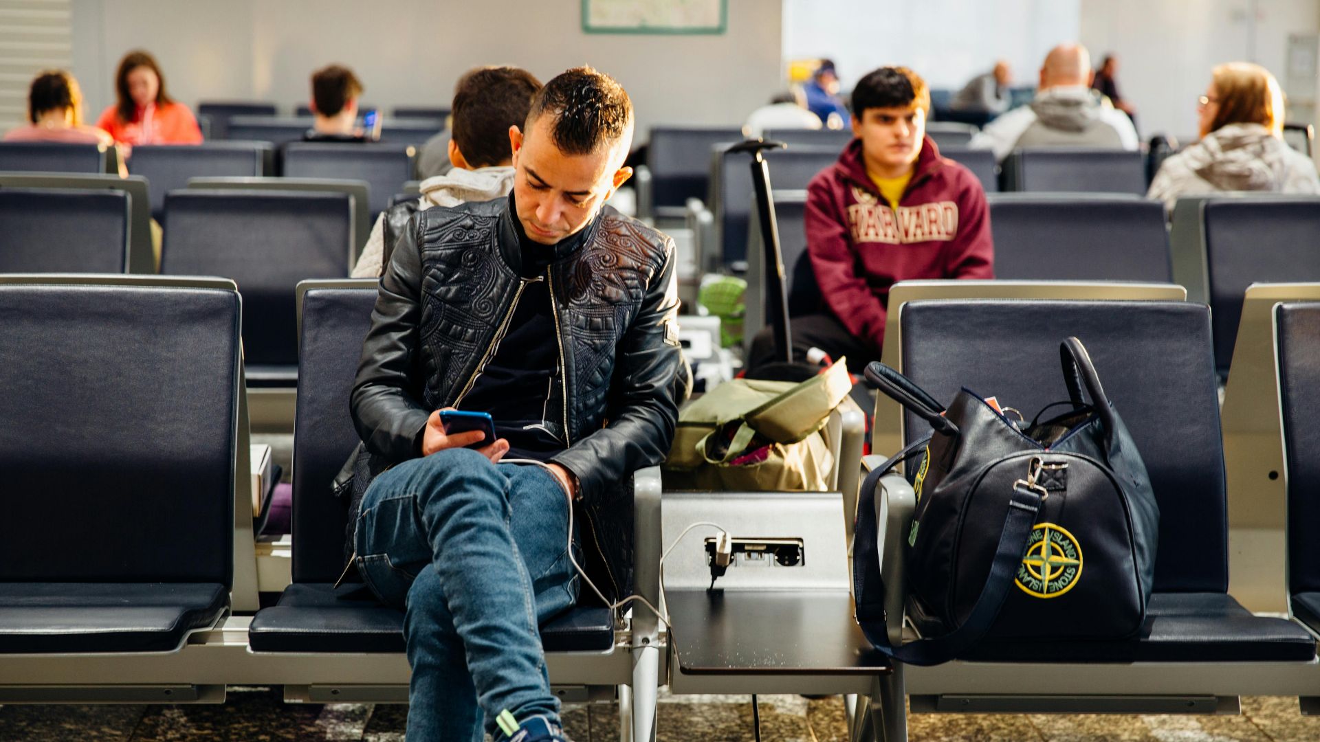 People sitting in an airport lounge, focused on smartphones and waiting for flights.
