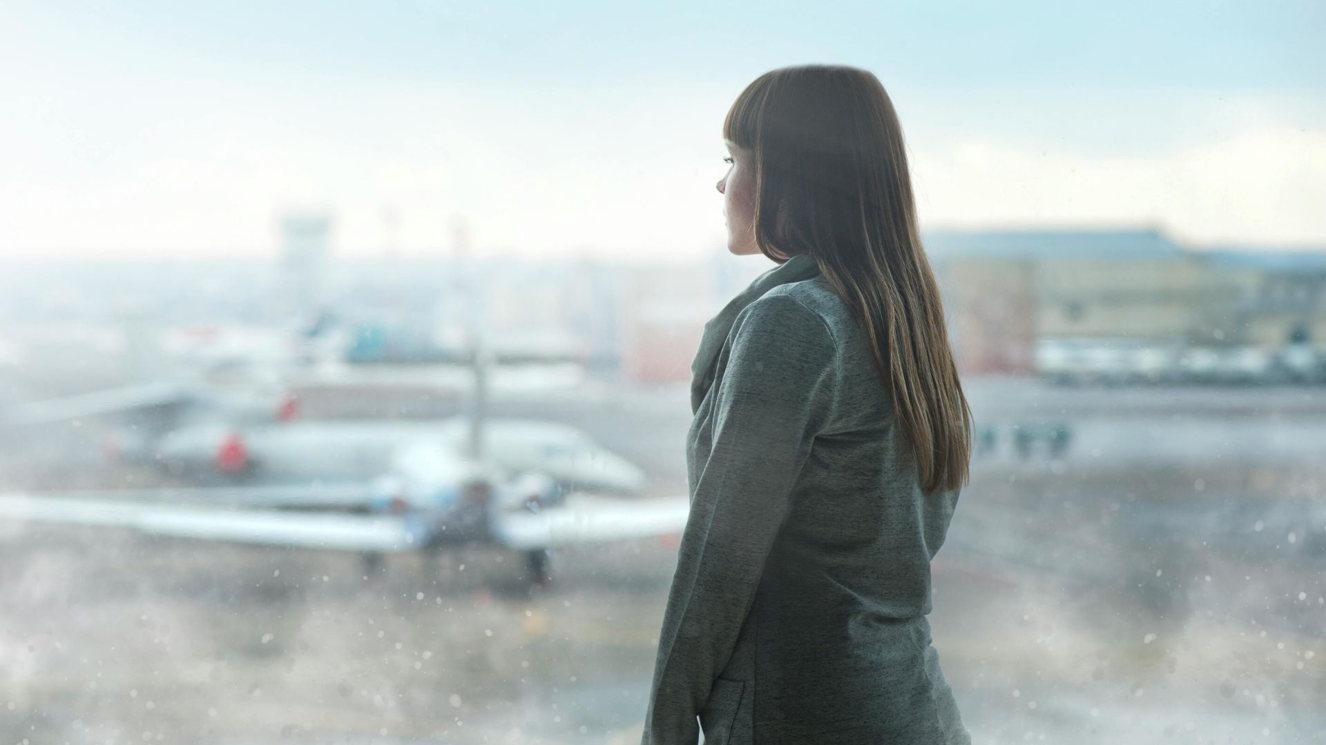 A woman gazing at airplanes through a window at Kyiv's airport terminal, capturing a moment of reflection.