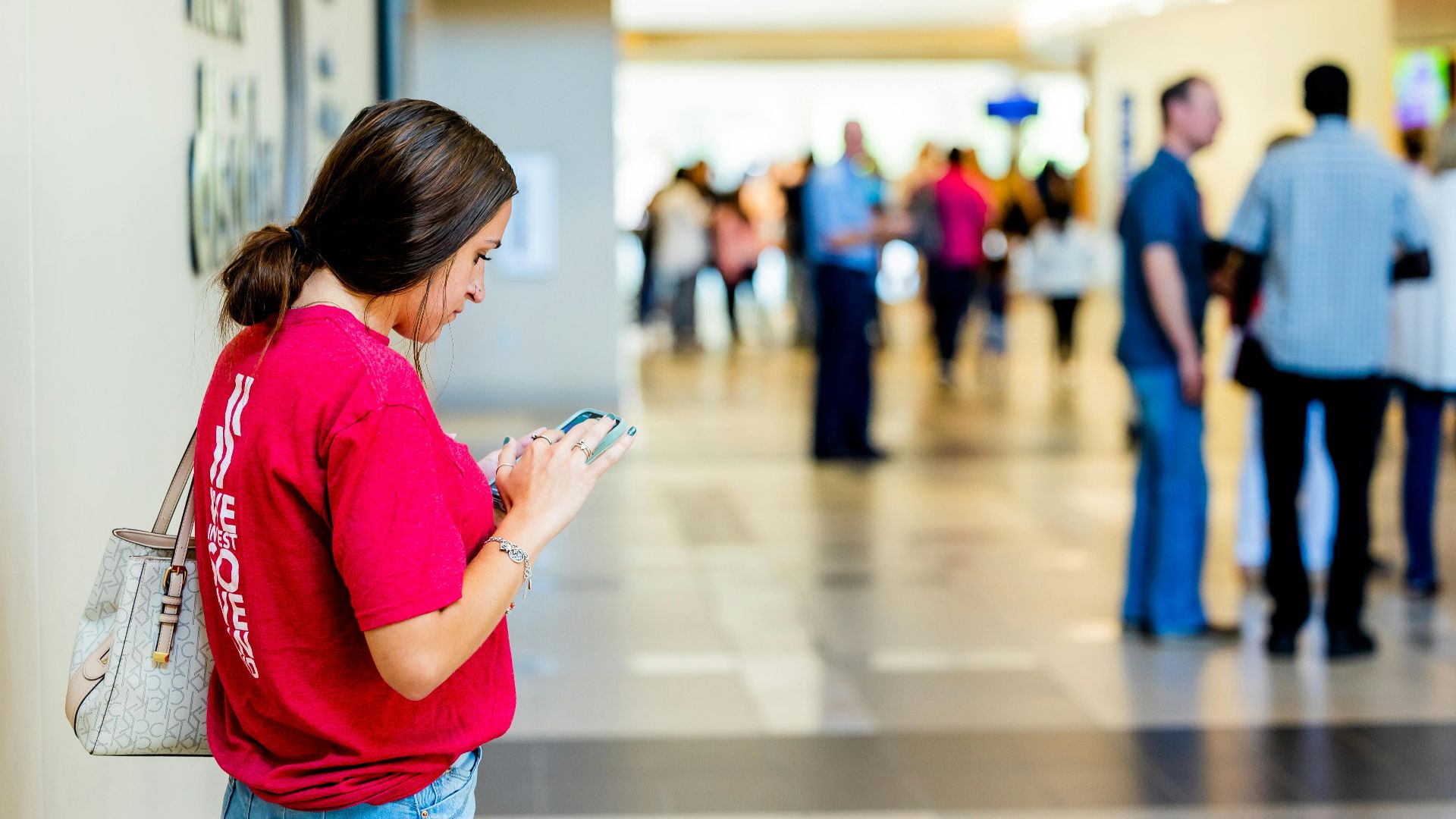 Young woman texting on smartphone in a bustling indoor corridor.