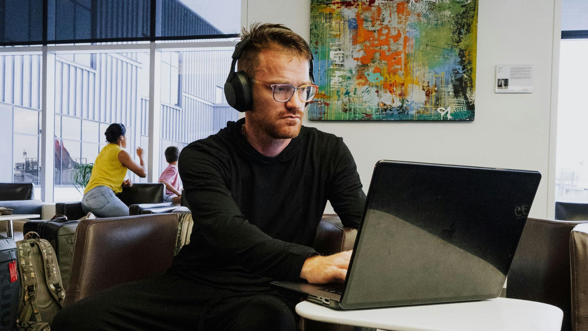 Business traveler wearing headphones works on laptop in airport lounge, focusing on productivity.
