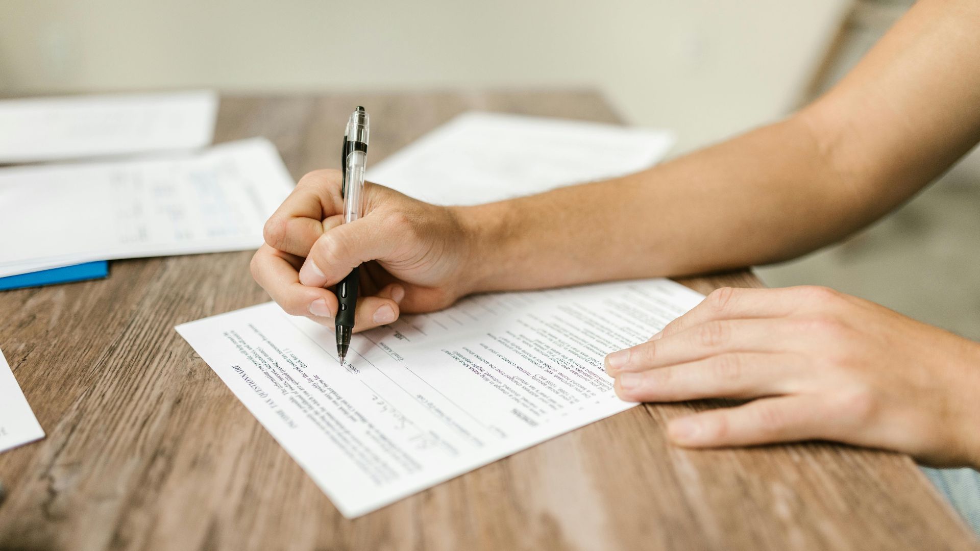 Hand filling out paperwork with a pen, showcasing focus on document completion.