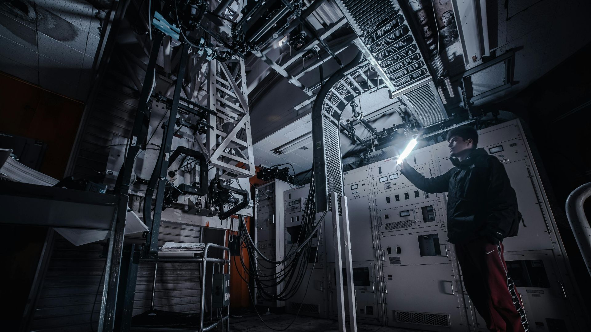 A technician using a flashlight to examine equipment in a dimly lit industrial control room.
