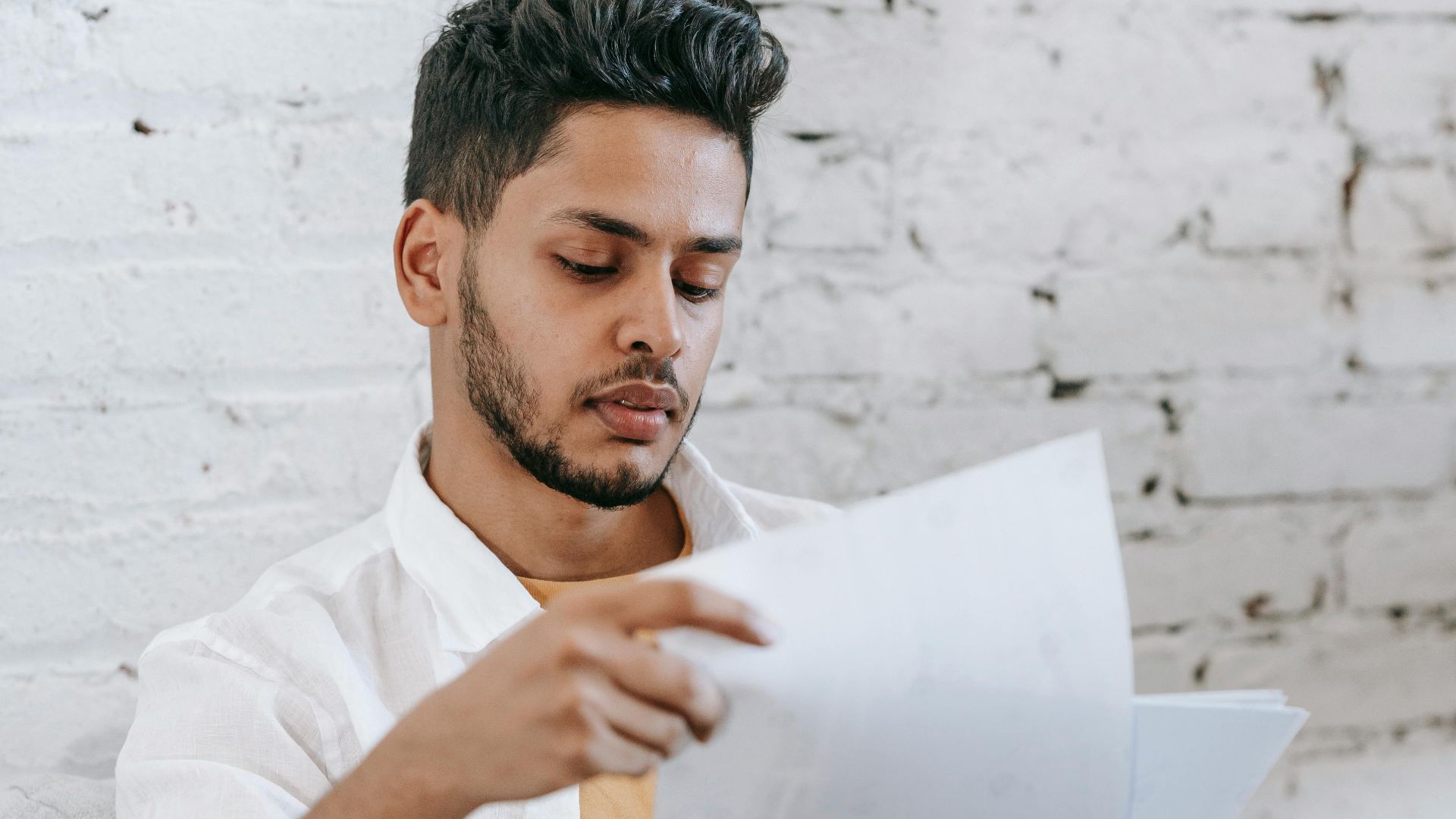 Concentrated young bearded Hispanic male sitting in armchair and analyzing contract while getting job offer