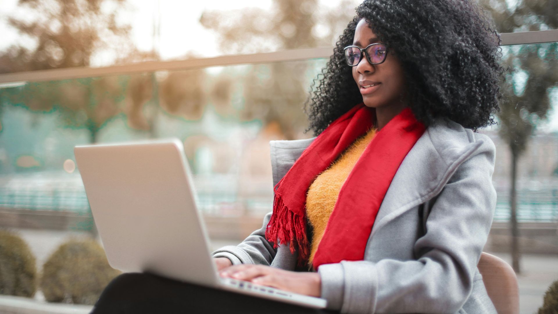 A woman working remotely on a laptop outdoors in a park setting. Stylish and focused.