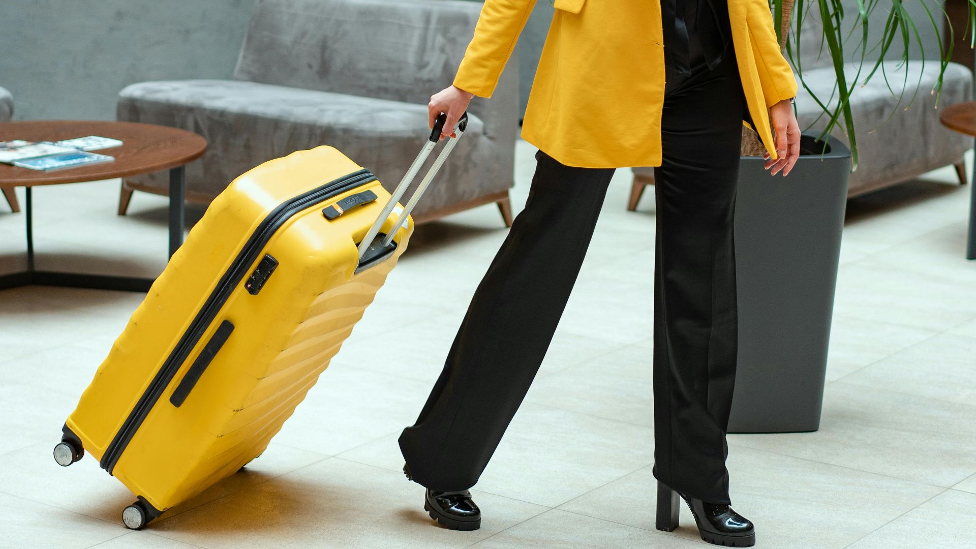 Stylish woman walking in hotel lobby pulling a bright yellow suitcase.
