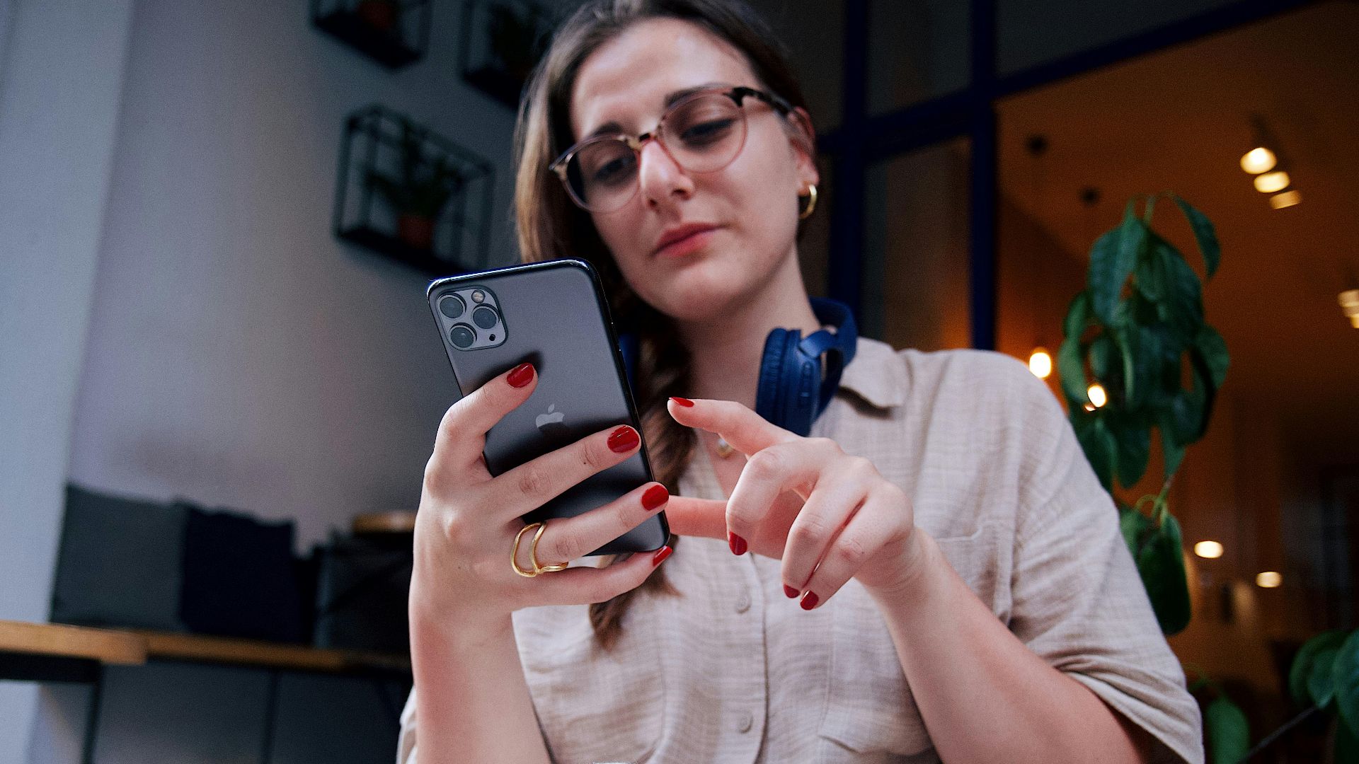 A young woman wearing eyeglasses uses a smartphone while relaxing in a modern café.