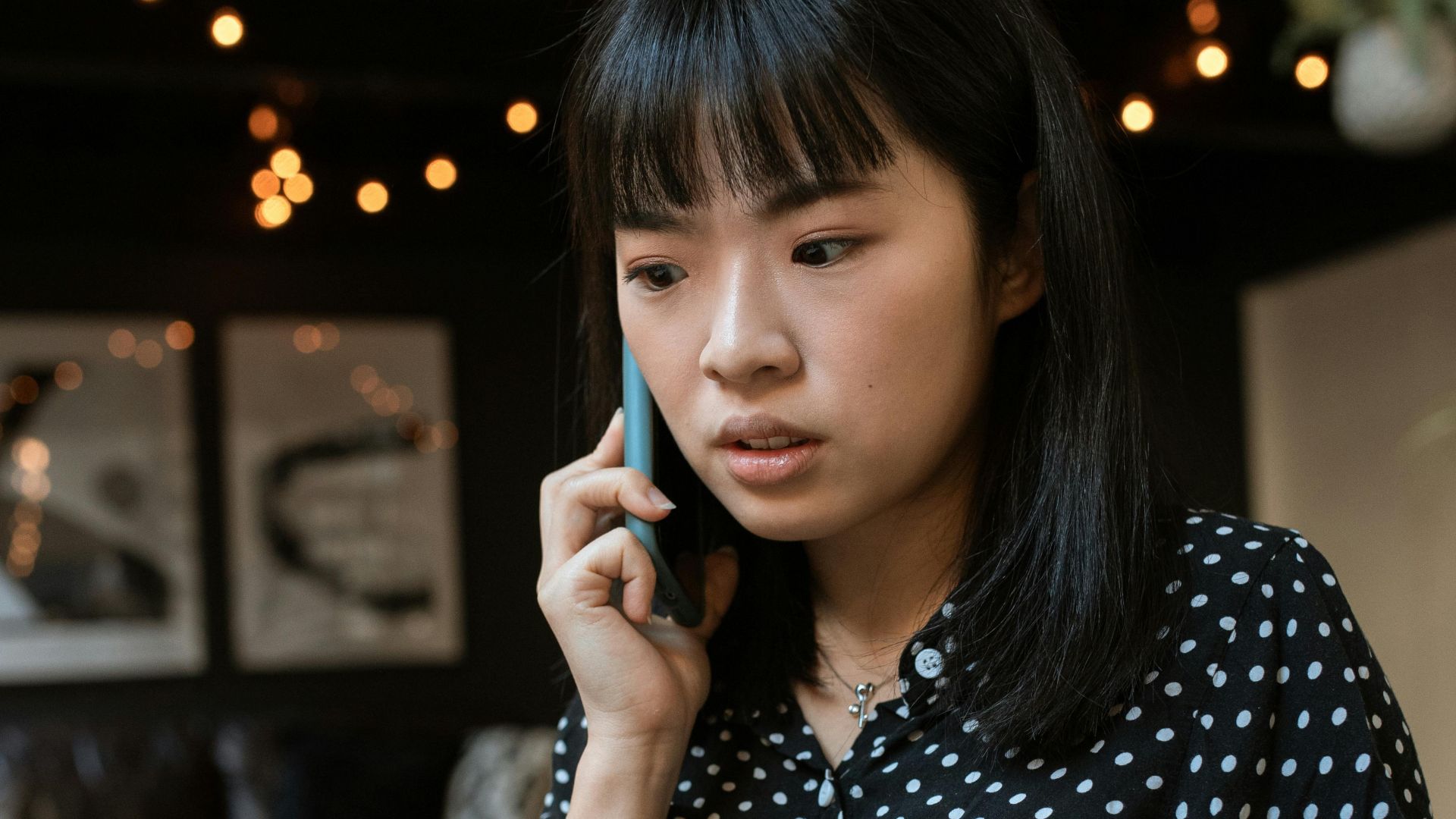 Focused young woman in a polka dot blouse taking a call indoors.