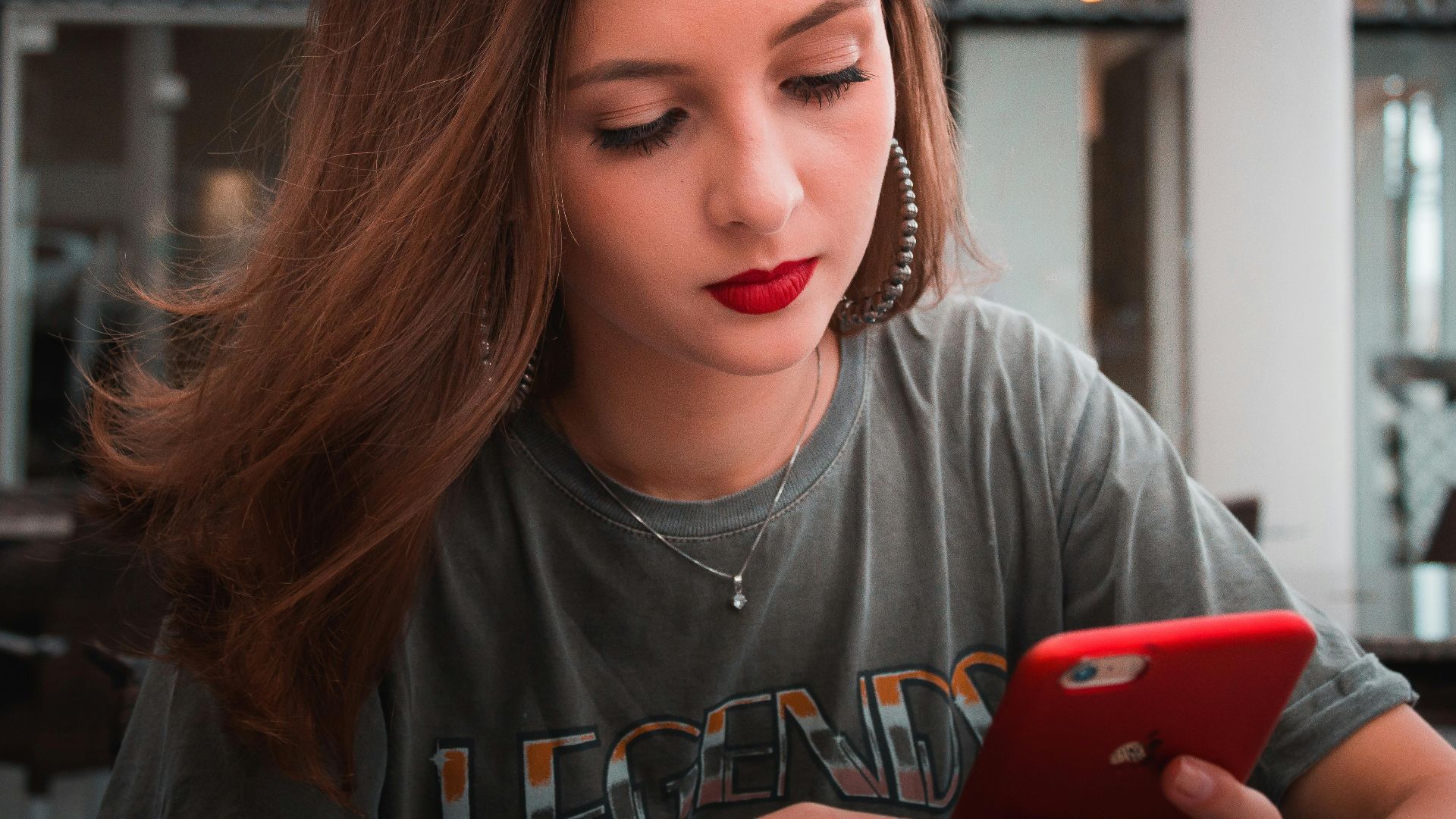 A young woman with red lipstick uses her phone in a modern cafe in Londrina, Brazil.