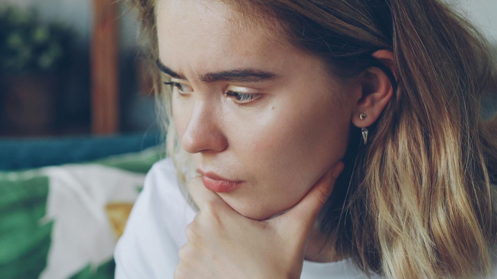 Young woman sitting indoors, holding a ring thoughtfully, looking pensive.