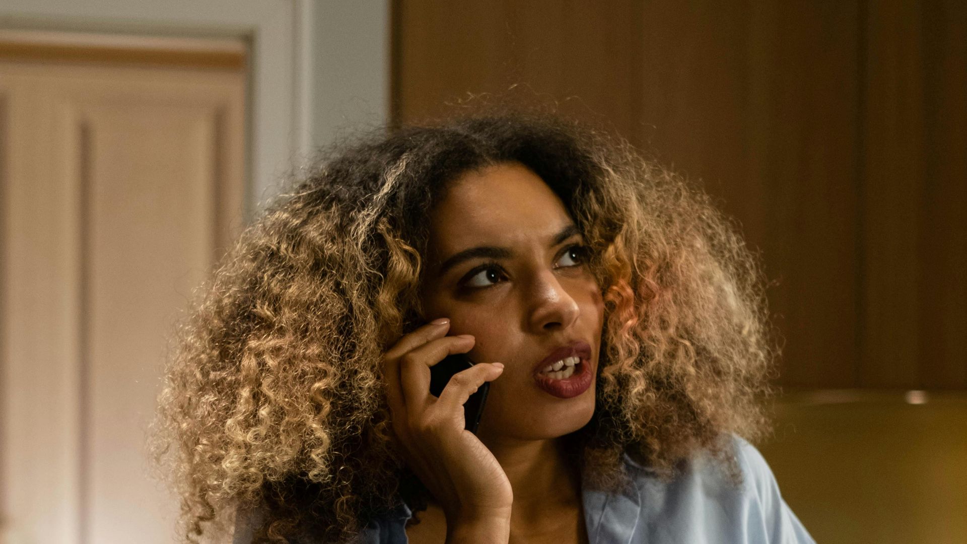 Adult woman with curly hair making a phone call indoors, lifestyle scene.
