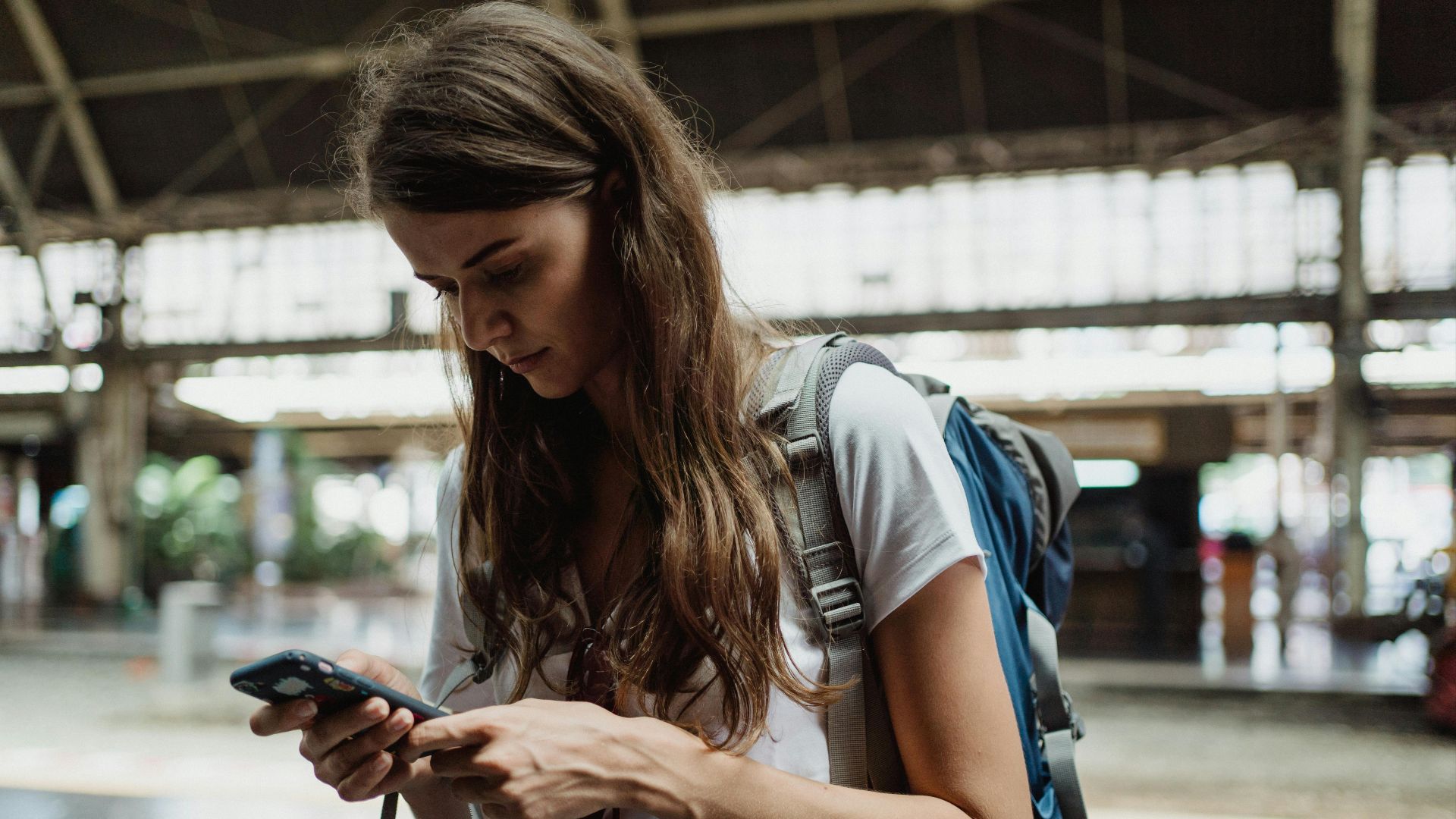 A young woman checks her smartphone while traveling at a train station.