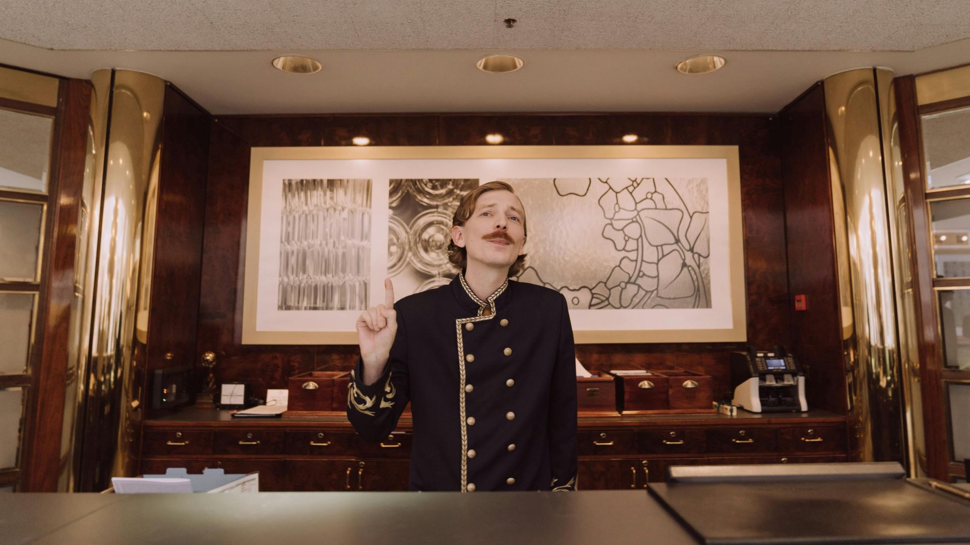 A luxury hotel receptionist in uniform stands behind the opulent front desk, ready to assist guests.
