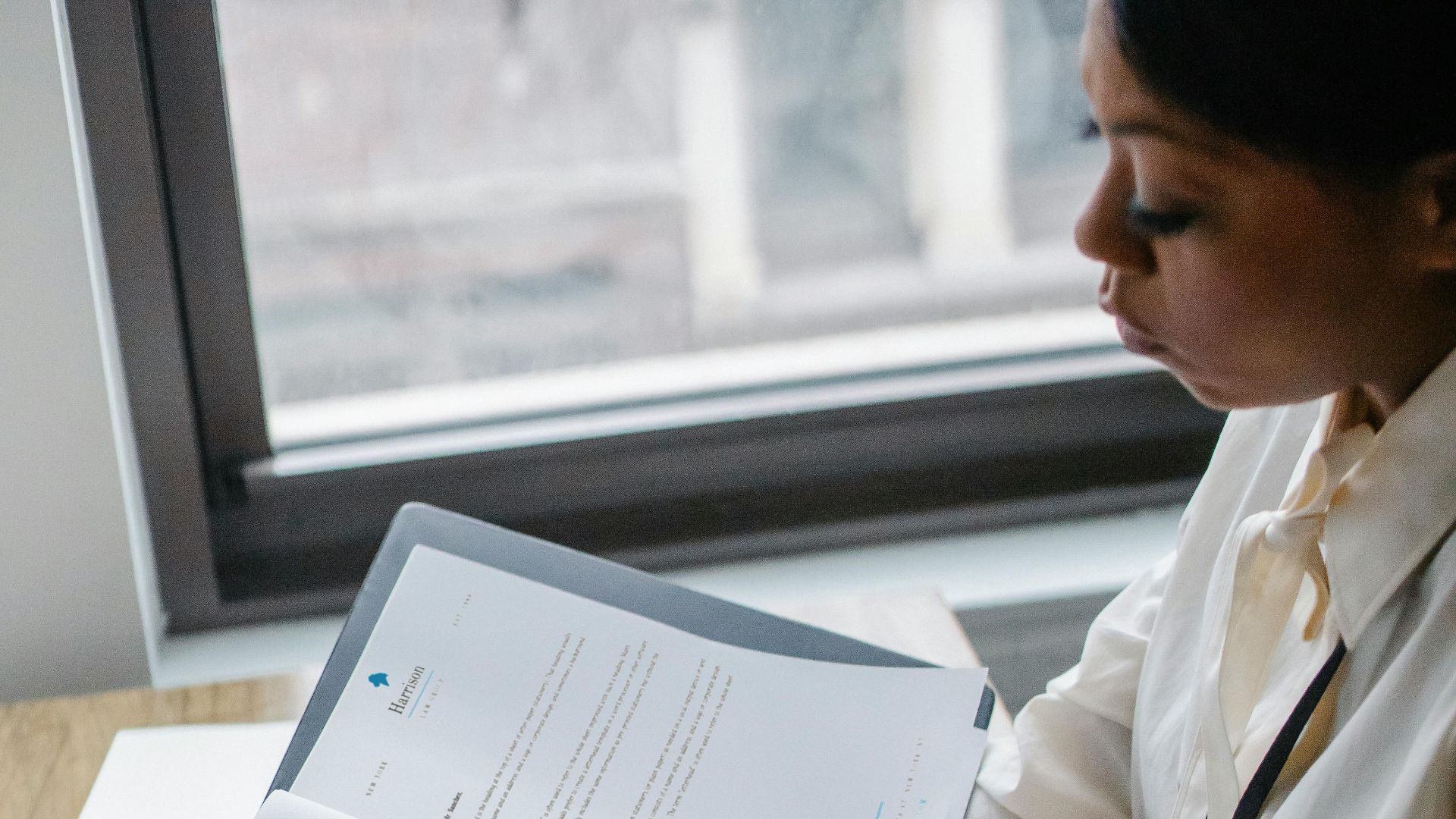 From above side view of crop African American female manager reading report of project while working with laptop in office