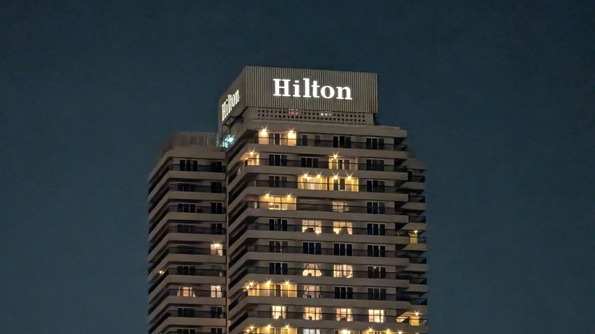 High-rise Hilton hotel building, illuminated at night against a clear sky. Ideal for cityscape and travel themes.