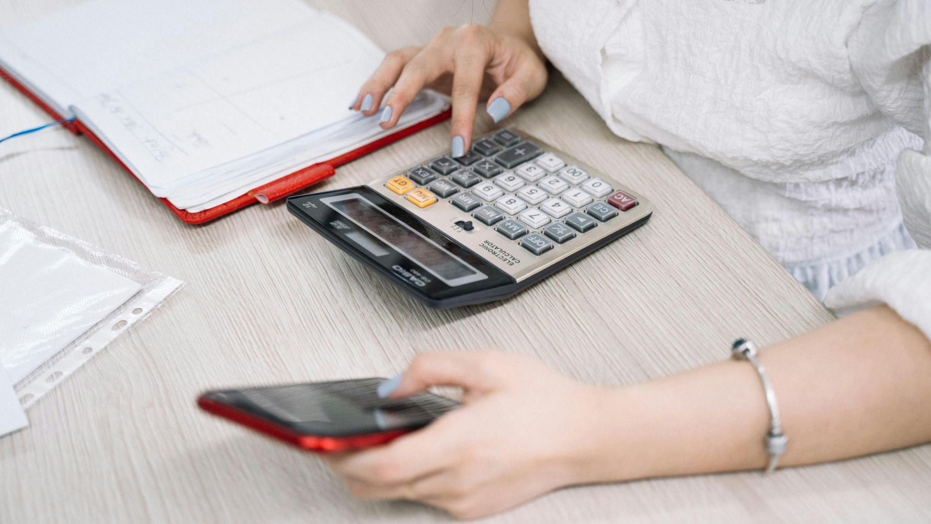 Close-up of a woman using a calculator and phone at her office desk.