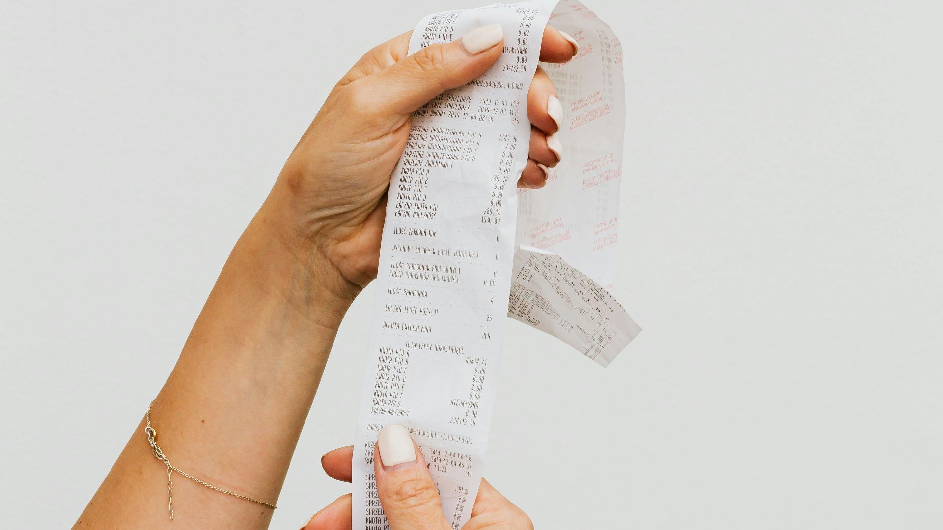 Close-up of woman's hands holding a long receipt against a white background, representing shopping or budgeting.