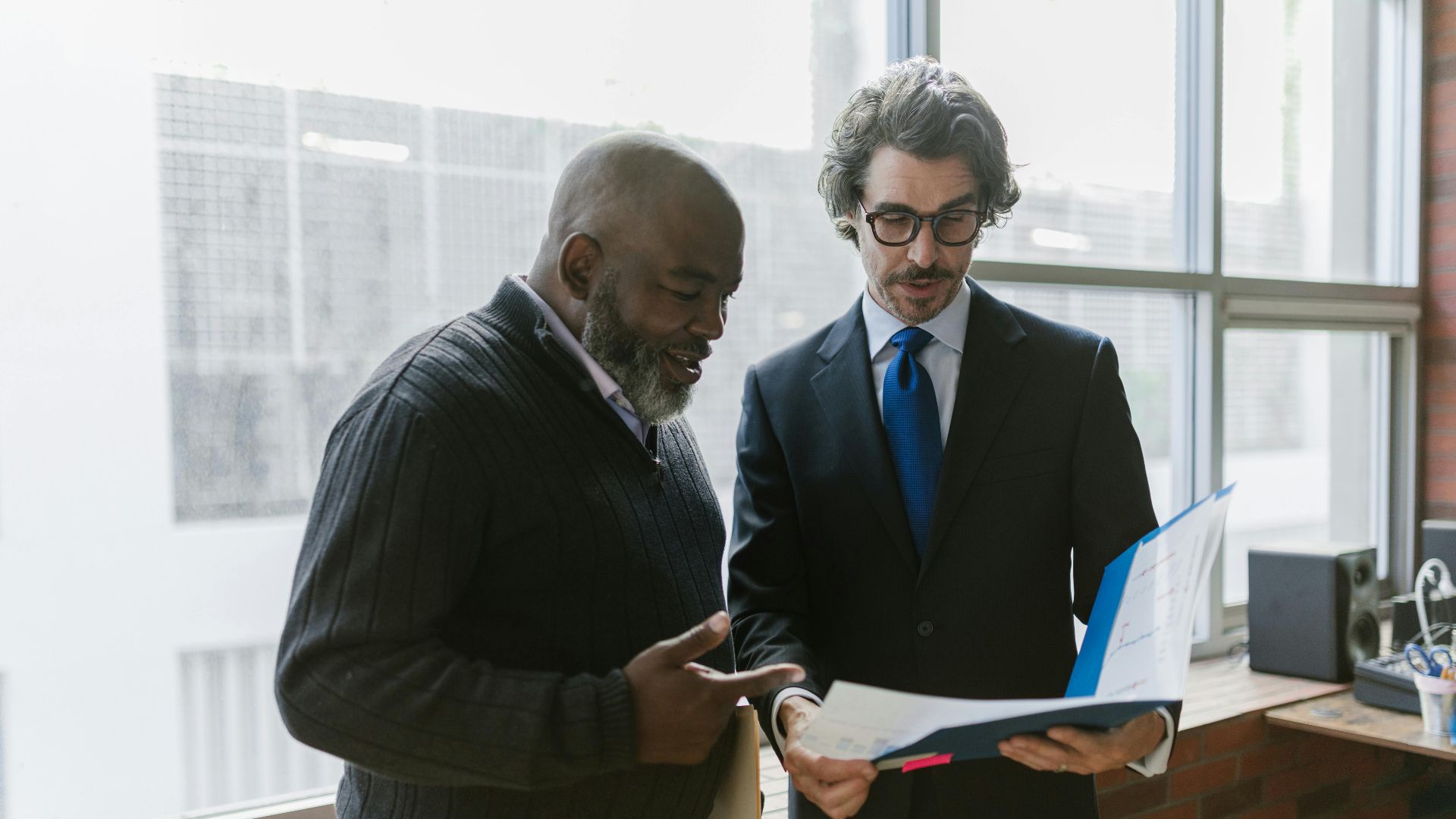 Two businessmen discussing and reviewing documents in a modern office setting.