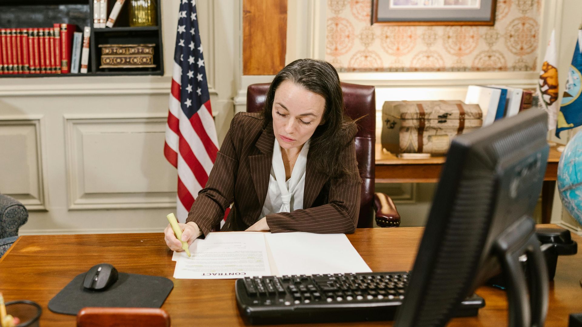 Female attorney in a law office signing legal documents at her desk, surrounded by legal books and symbols of justice.