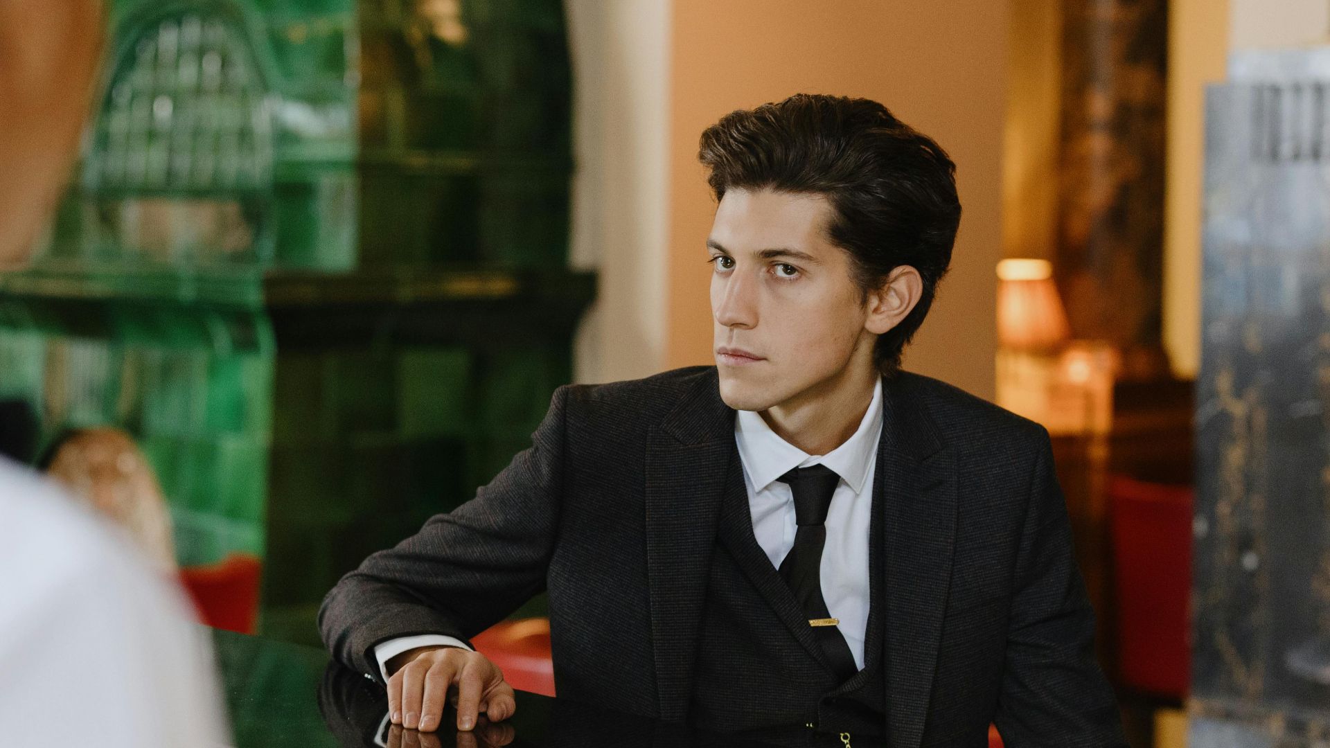 Sophisticated man in a suit sitting at a vintage bar counter indoors, exuding elegance and style.