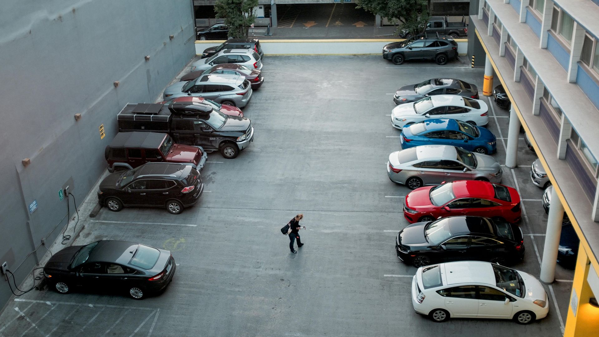 A man walks in a city parking lot filled with various cars, offering a busy urban scene.