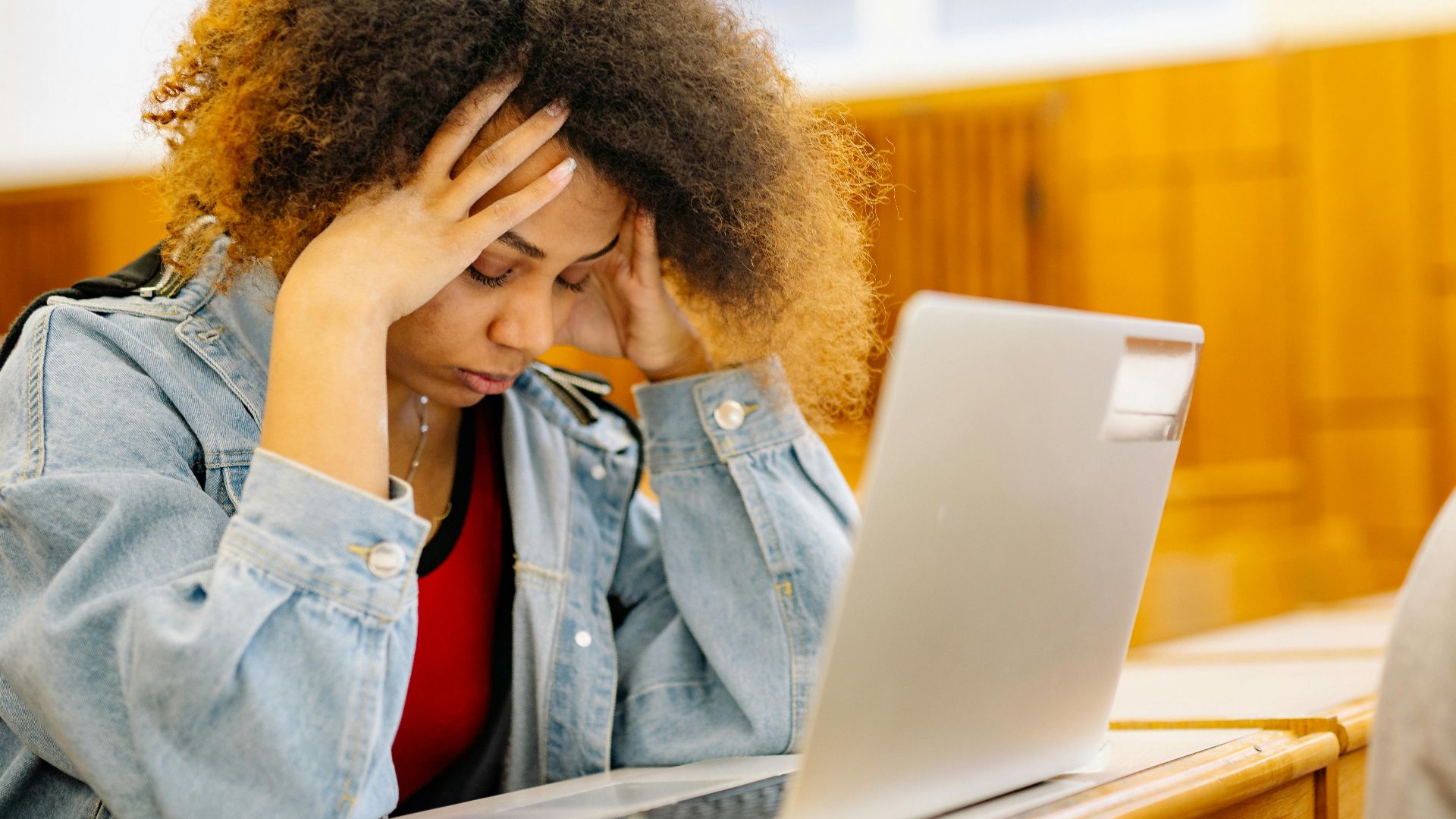 A young woman experiencing a headache while studying with a laptop indoors, looking stressed and overwhelmed.