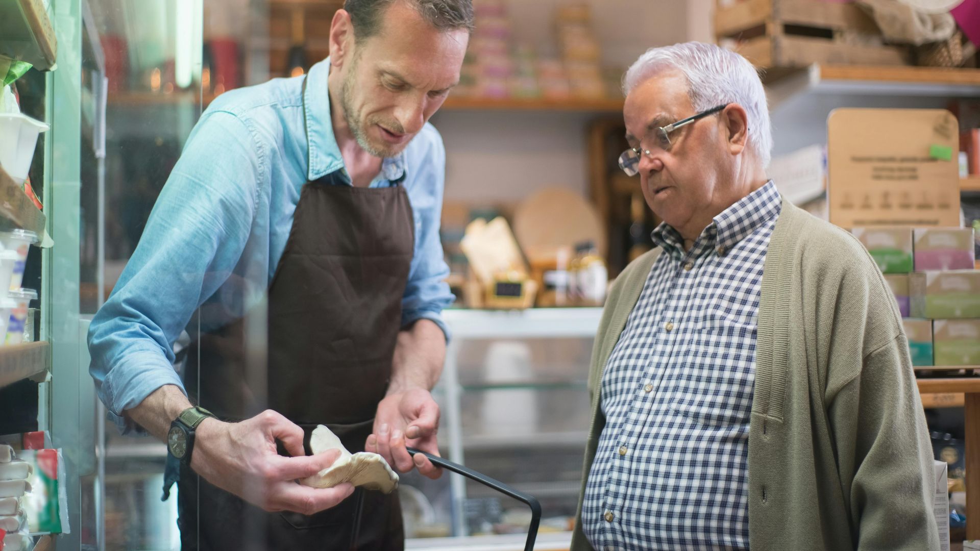 Friendly grocery store interaction between a salesman and senior customer in Portugal.