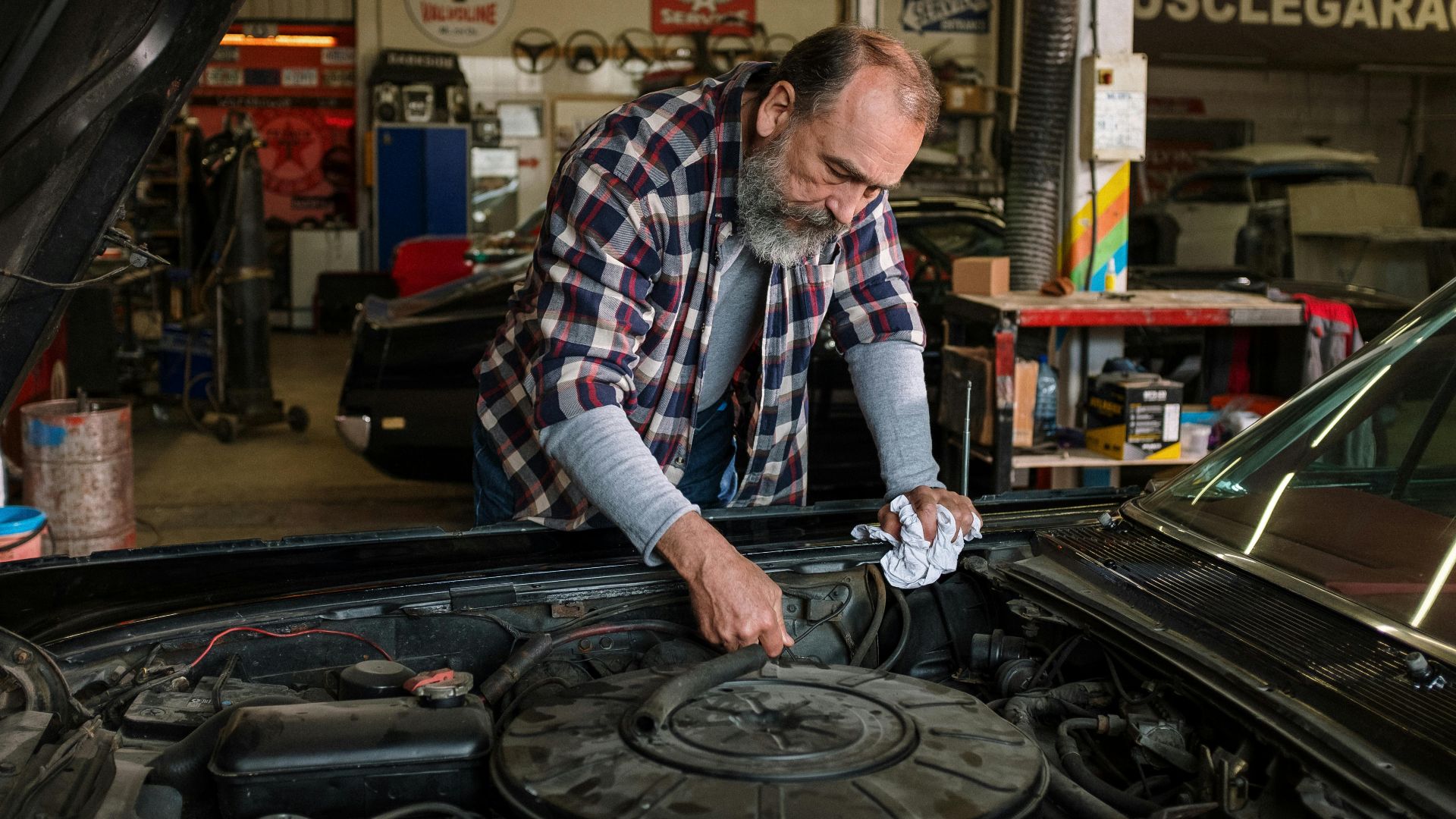 Bearded mechanic working on engine repair in an auto repair shop garage with a focus on hands-on car service.