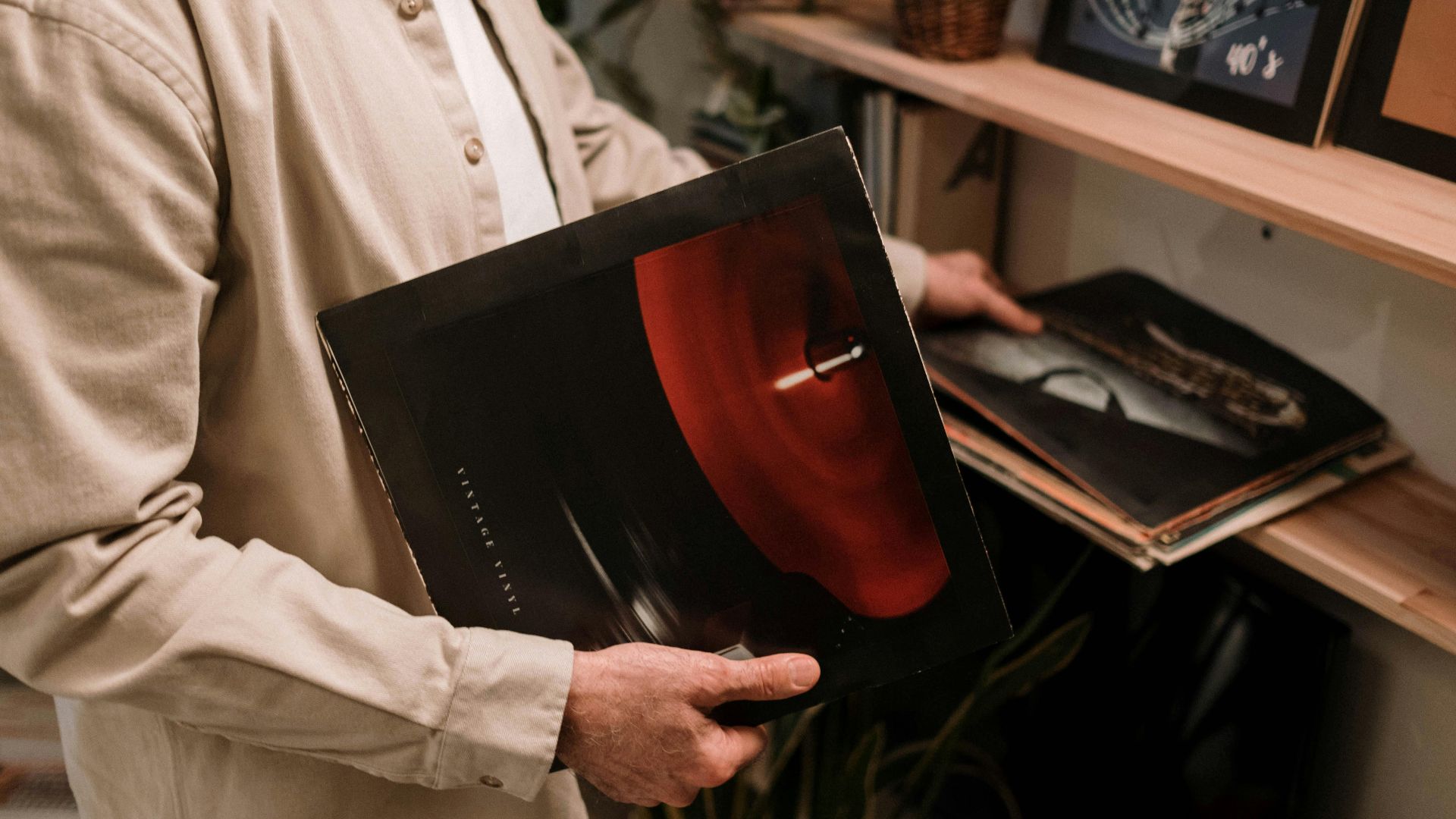 Adult holding vintage vinyl record, browsing a collection on a shelf indoors.