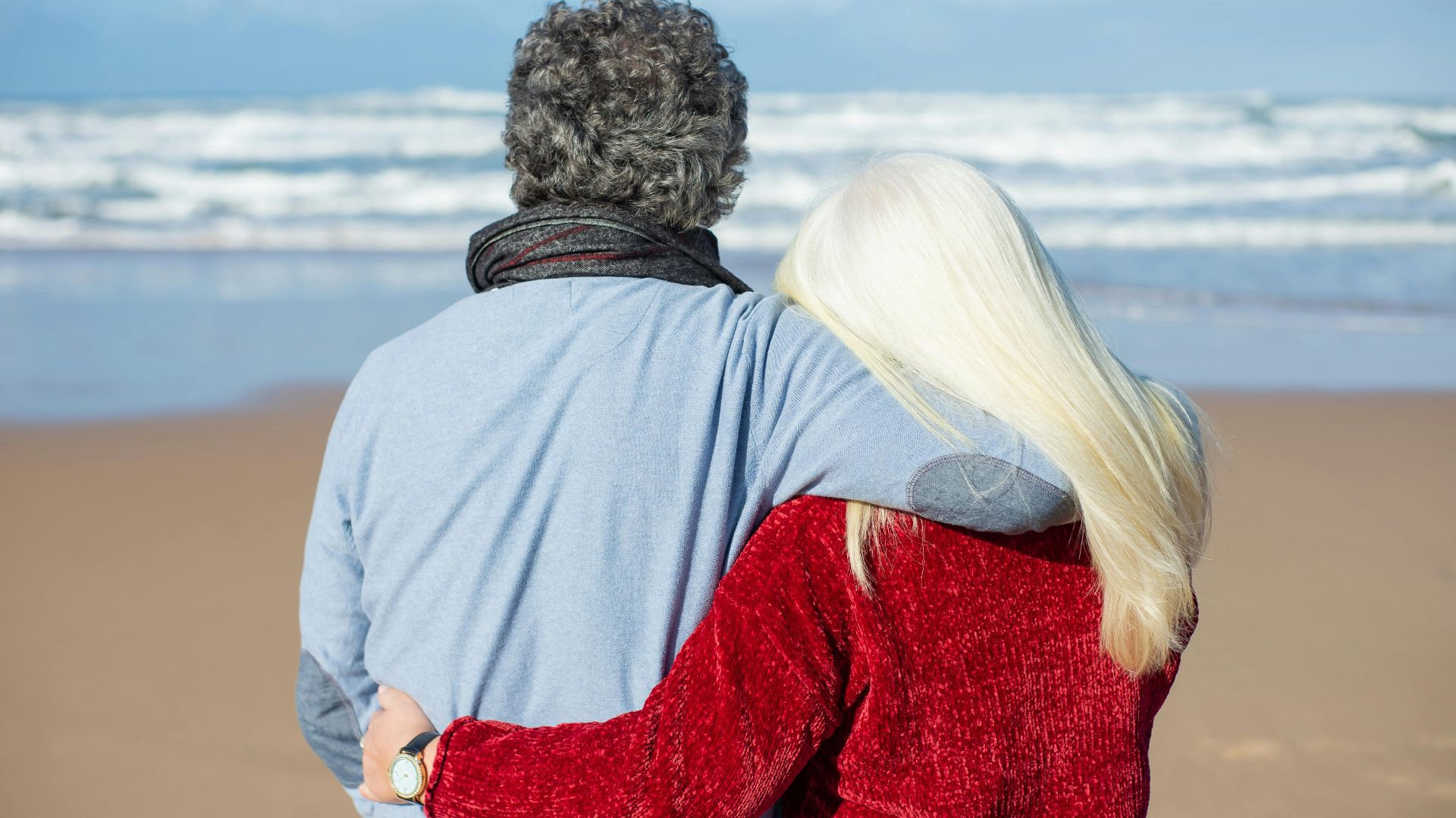 An elderly couple embraces while enjoying the sea view on a Portuguese beach.